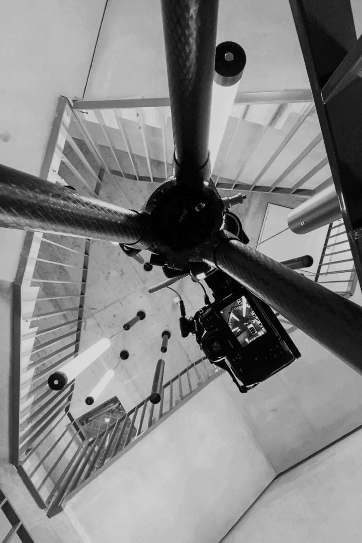 Fotografie einer Kamera, die auf einem Stativ an einer Treppe im Innenbereich zeigt, schwarz-weiß, modernes Design.