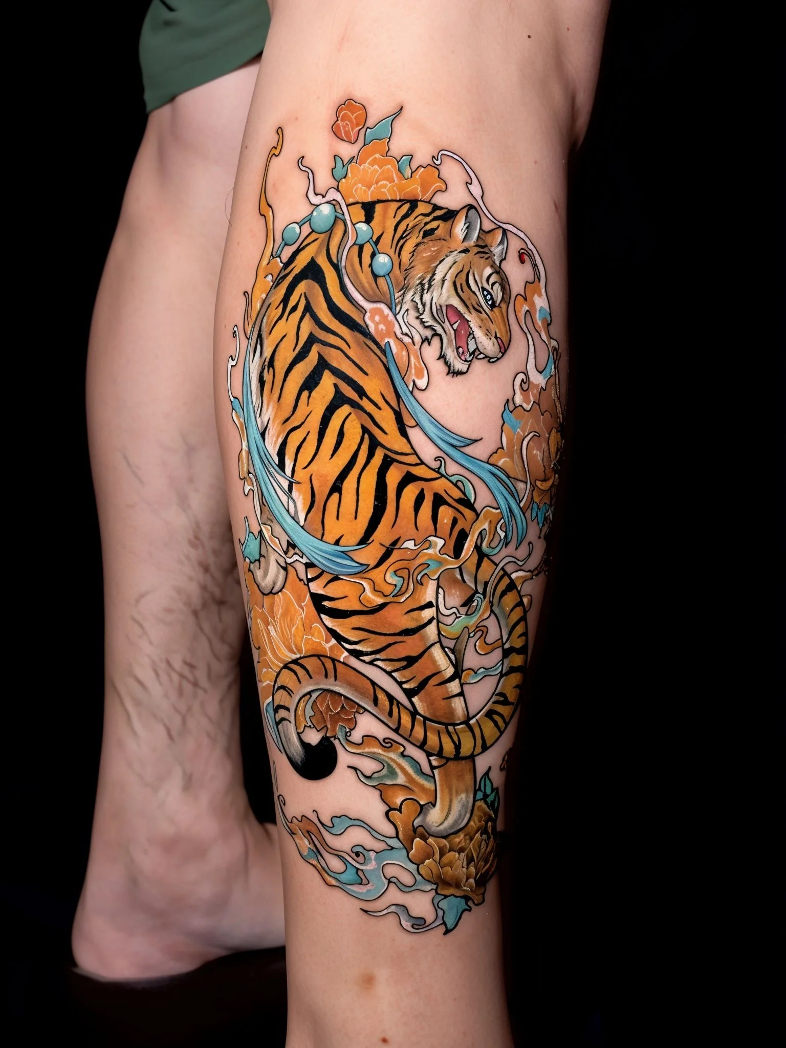 Tattoo of a tiger with blue water and orange flowers on a person's thigh.