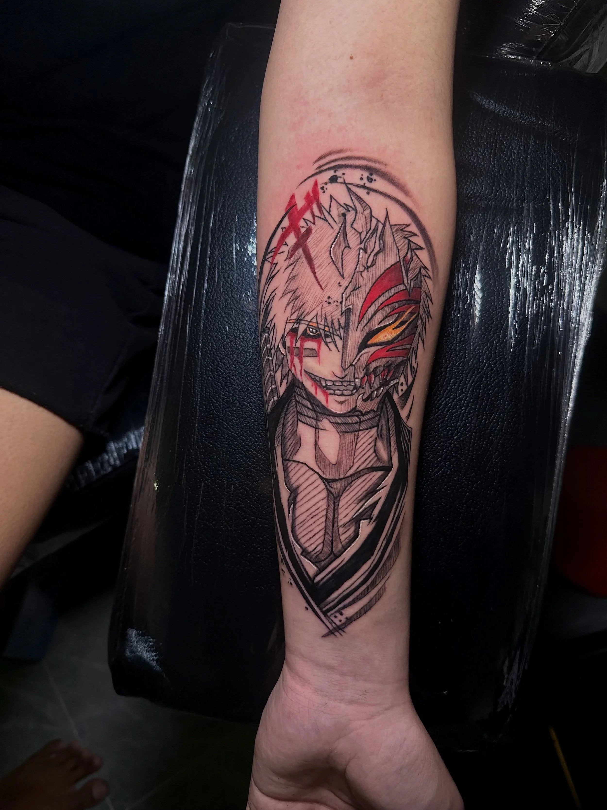 Tattoo of a manga-style character with blonde hair, a half white and half demon face, and a mischievous smile on an arm.