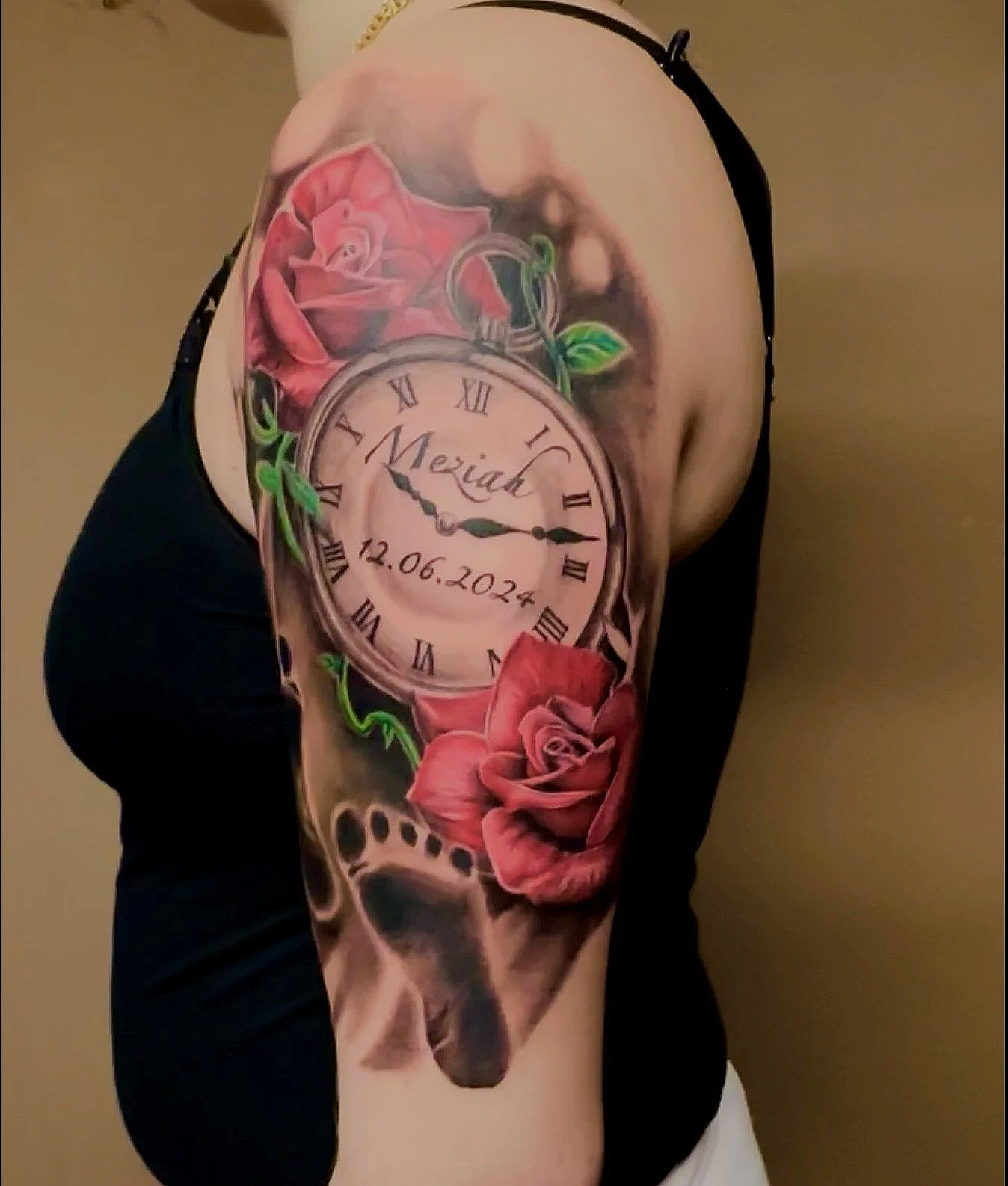 A tattoo featuring a pocket watch with Roman numerals, the name 'Meriad,' and the date '12.06.2024,' surrounded by pink roses, green leaves, and a dog skull at the bottom.