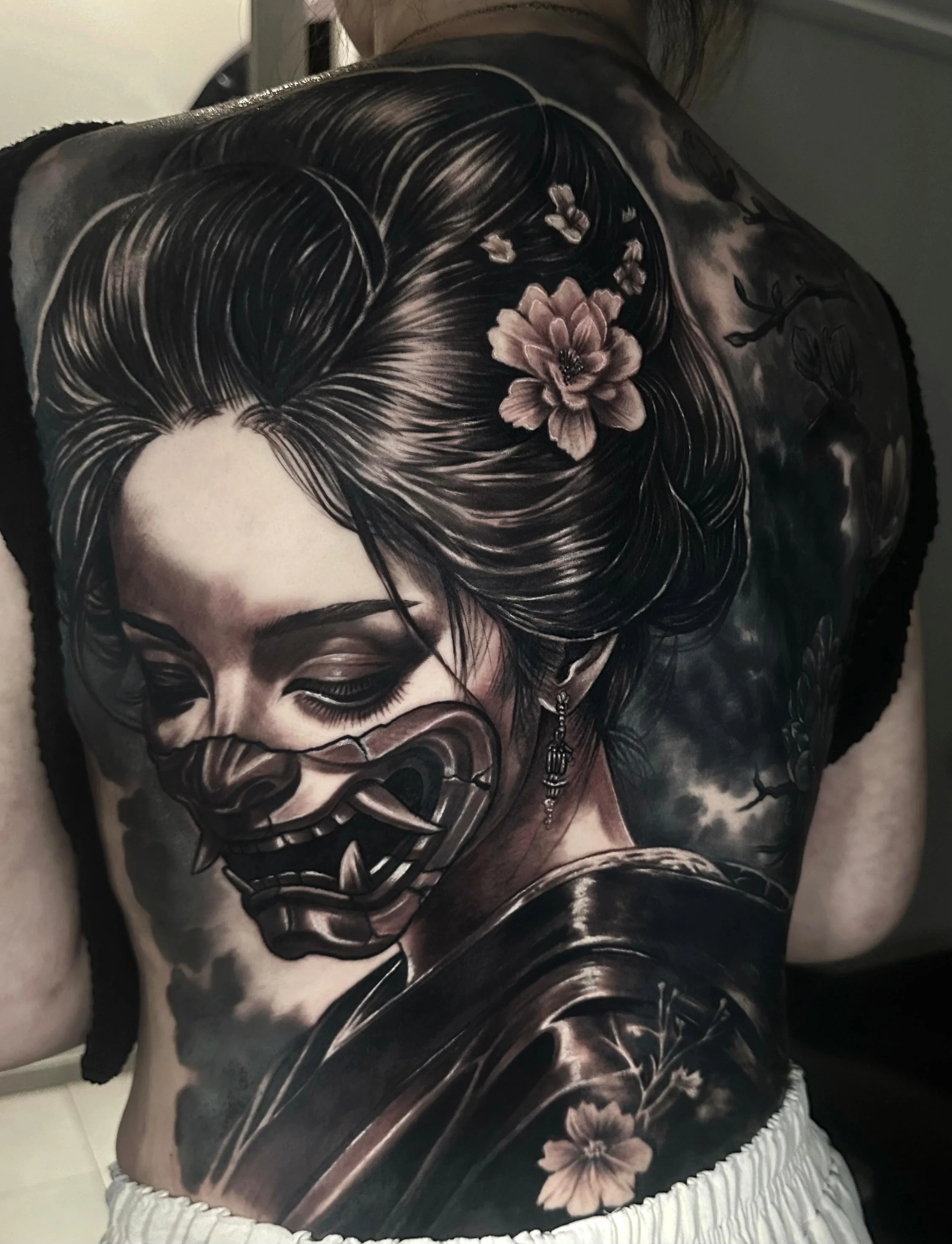 A detailed tattoo of a woman's face, with her hair adorned with flowers and branches, covers the person's shoulder and upper arm.