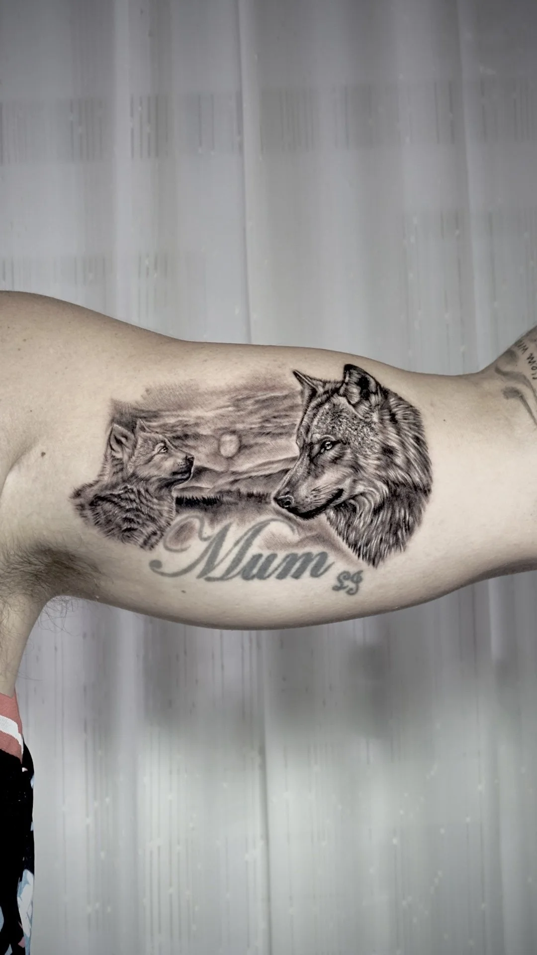 Tattoo of two wolves facing each other with a landscape background and the word "Mum" in cursive below.