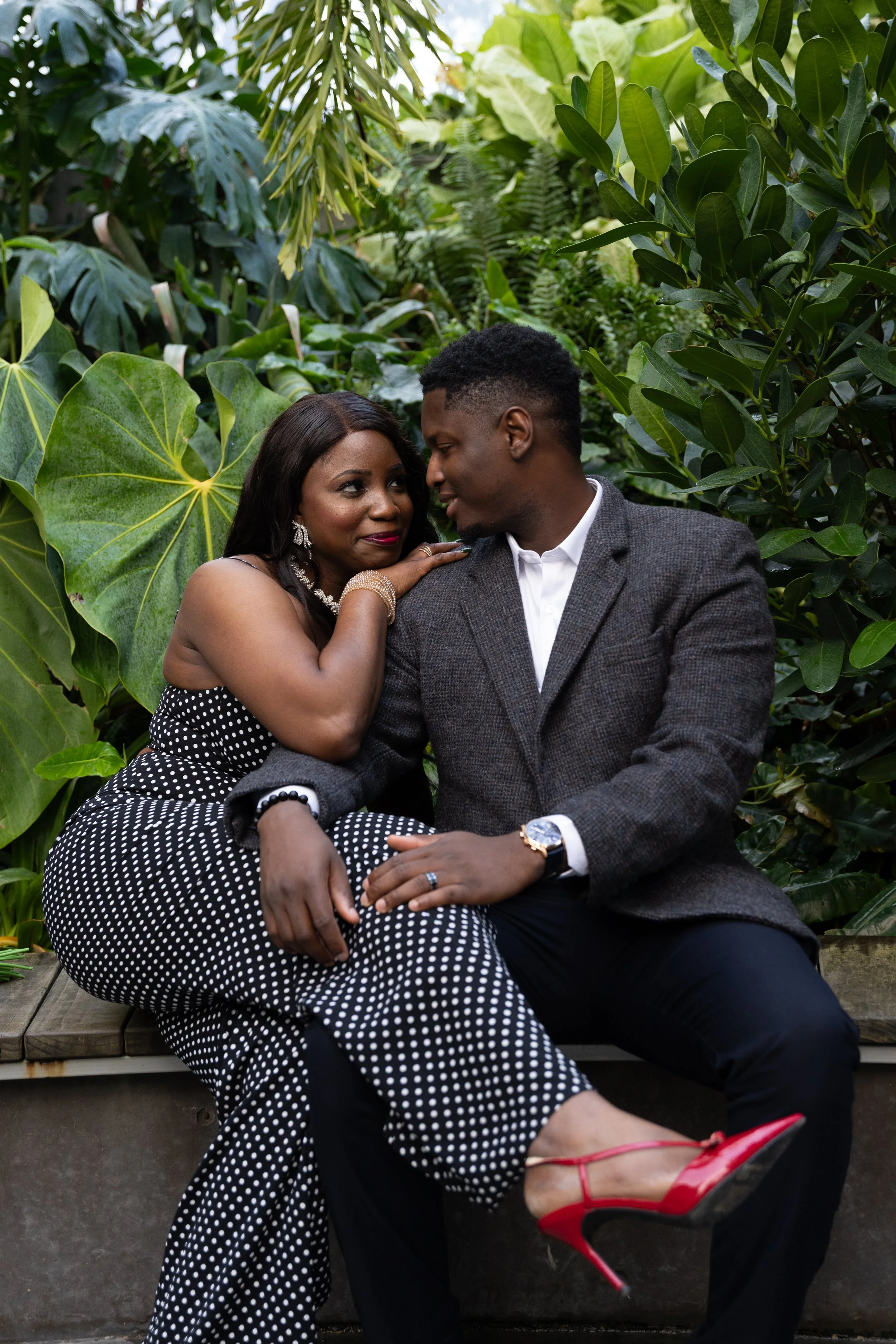 A couple sitting closely on a bench surrounded by lush green plants, sharing an intimate moment.