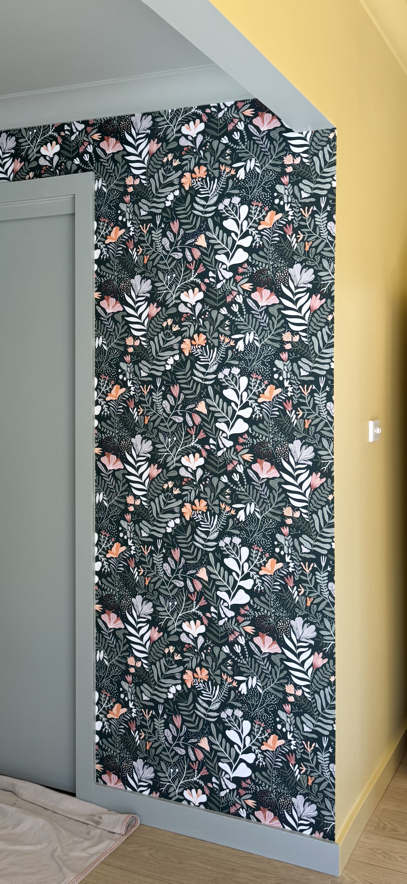 Interior wall with floral wallpaper featuring dark background and pink, white, and peach flowers, with a light green door and yellow wall nearby.