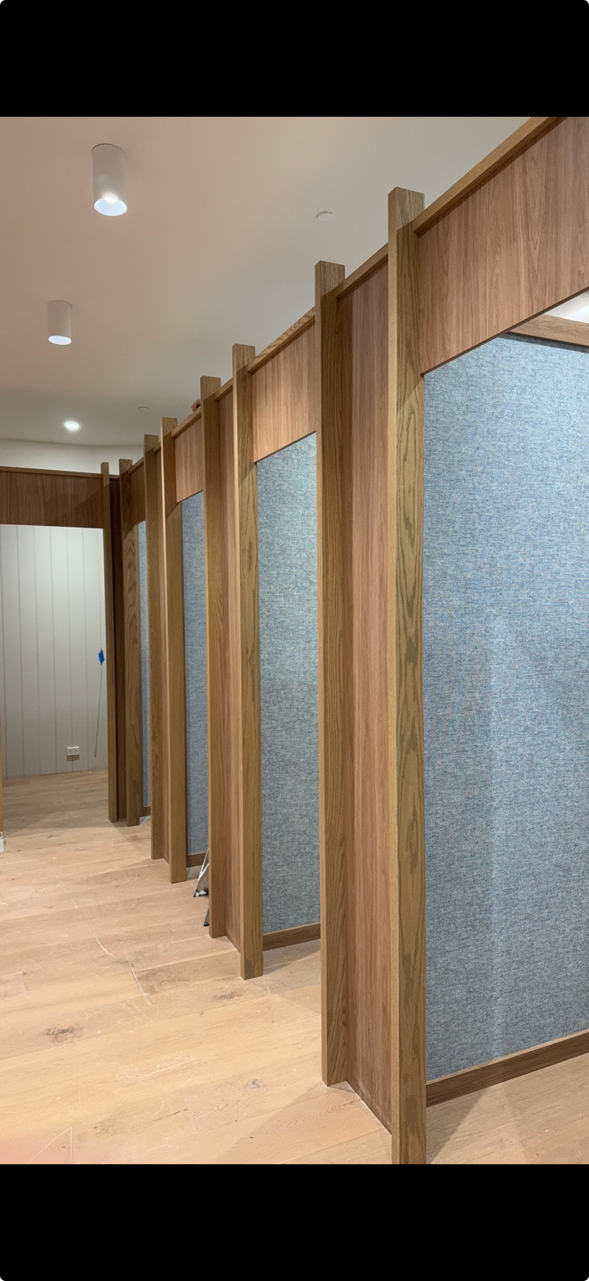 Interior view of privacy stalls with wooden frames and fabric panels, in a modern restroom or changing room.