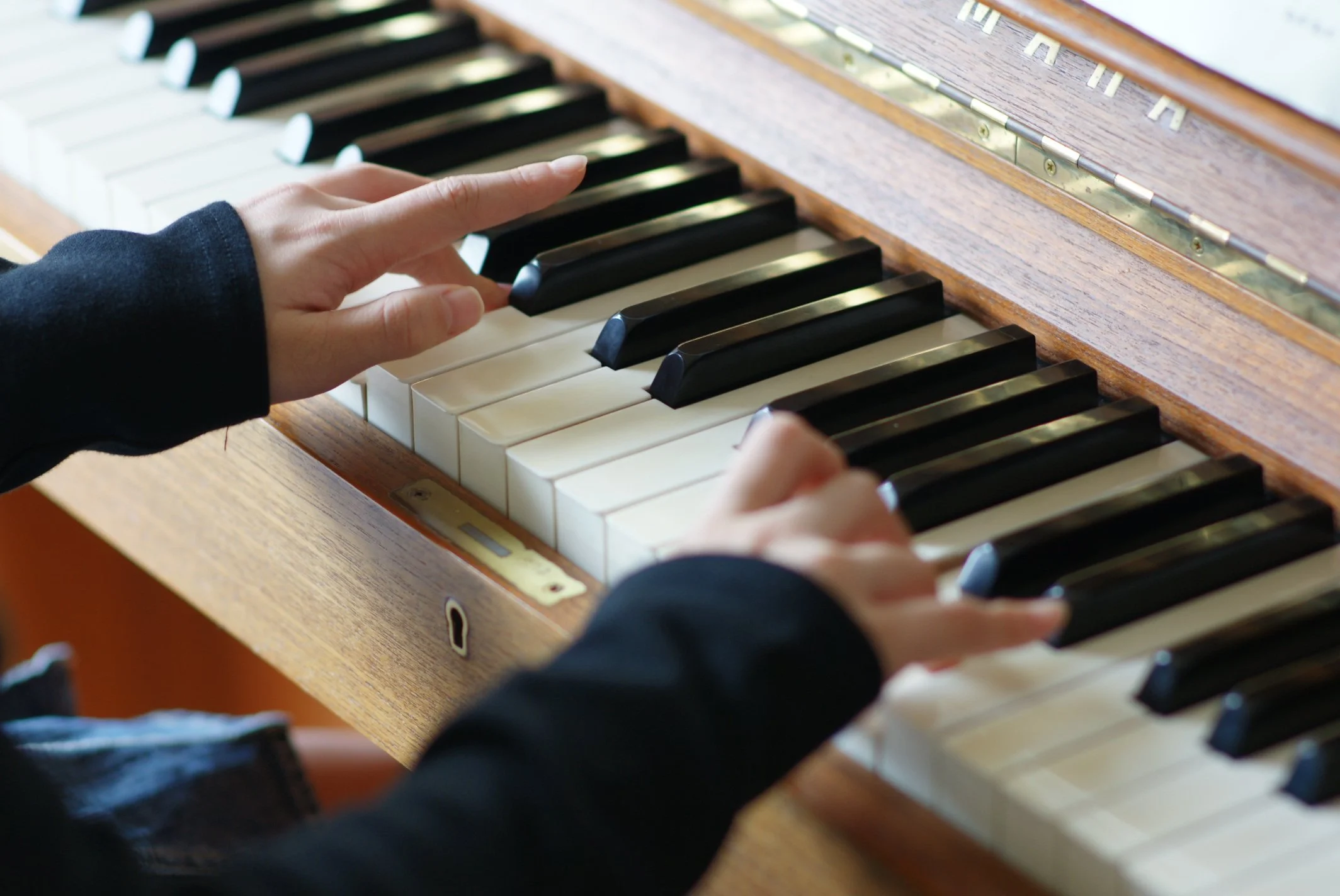 Person playing a piano, focusing on hands pressing black and white keys on a wooden keyboard.