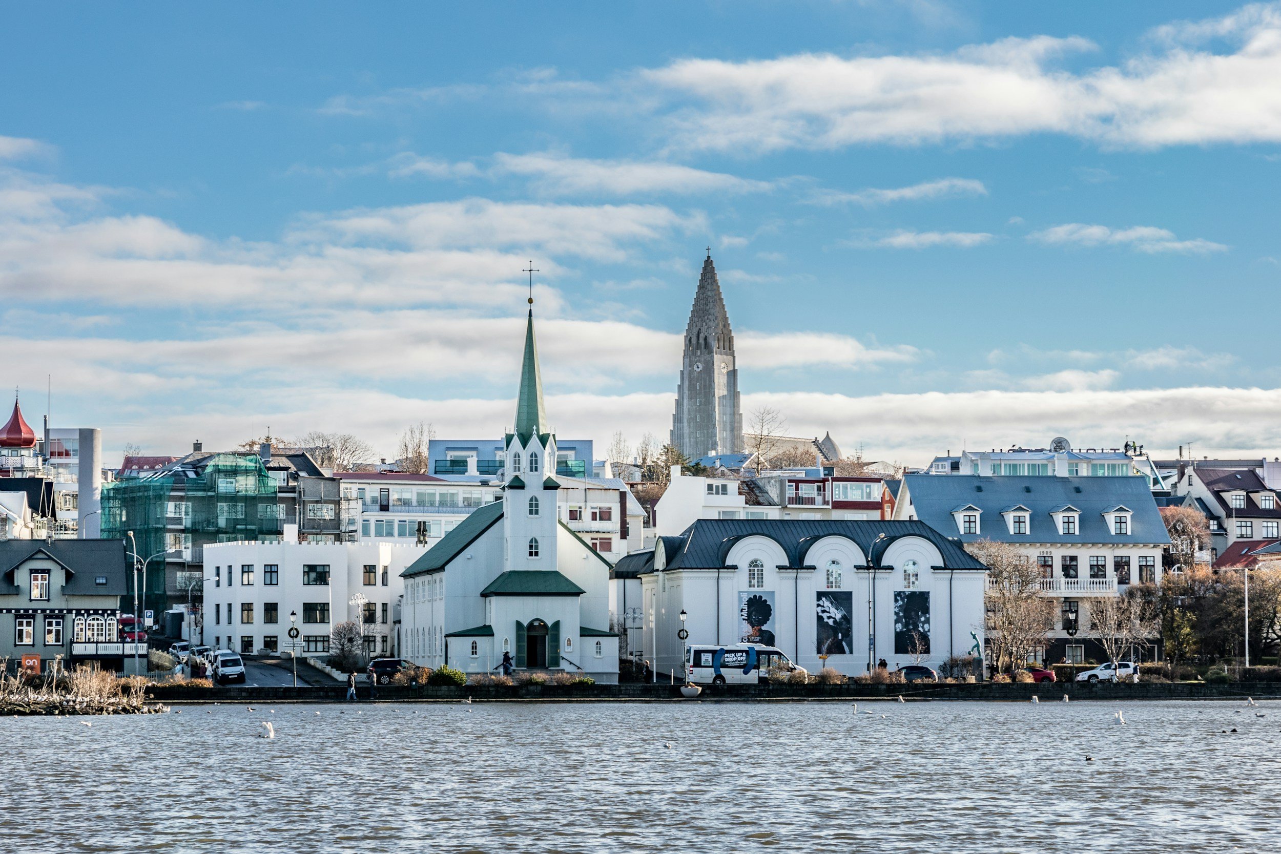 Cityscape with a church, various buildings, and a body of water in the foreground on a clear day.