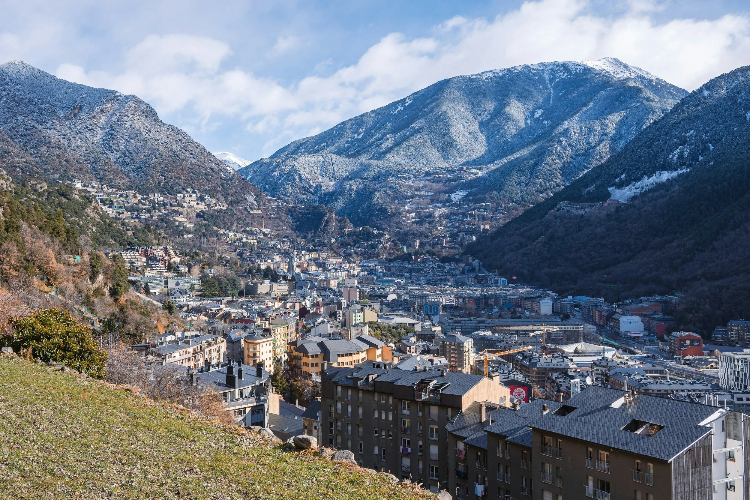 Mountain town with snow-capped mountains in the background, residential buildings in the foreground, and partly cloudy sky.
