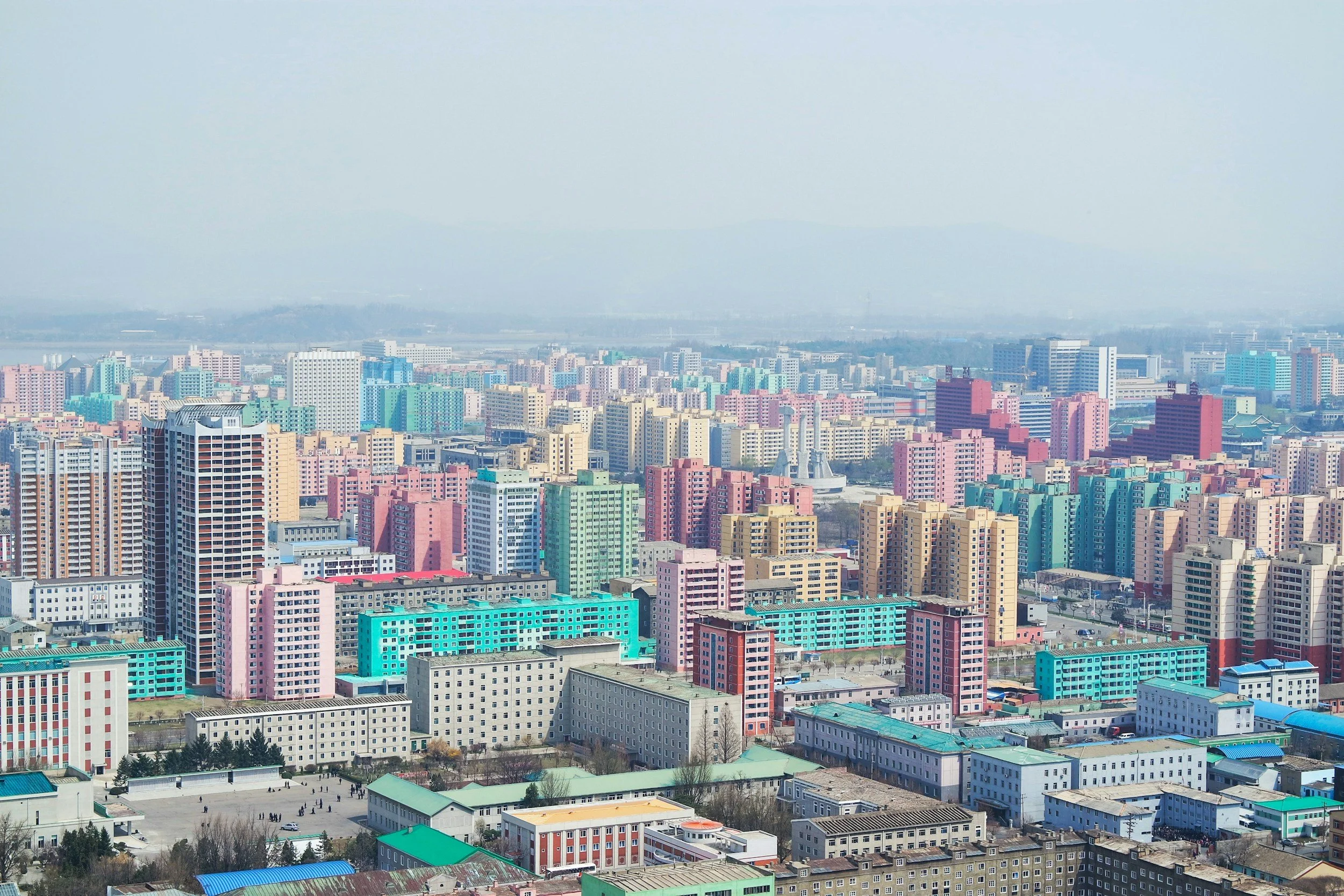 A city skyline featuring numerous colorful high-rise buildings and apartment complexes under a hazy sky.