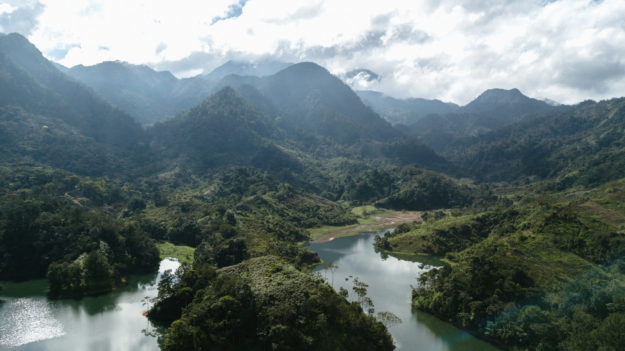 Scenic view of a river flowing through lush green mountains with clouds overhead.