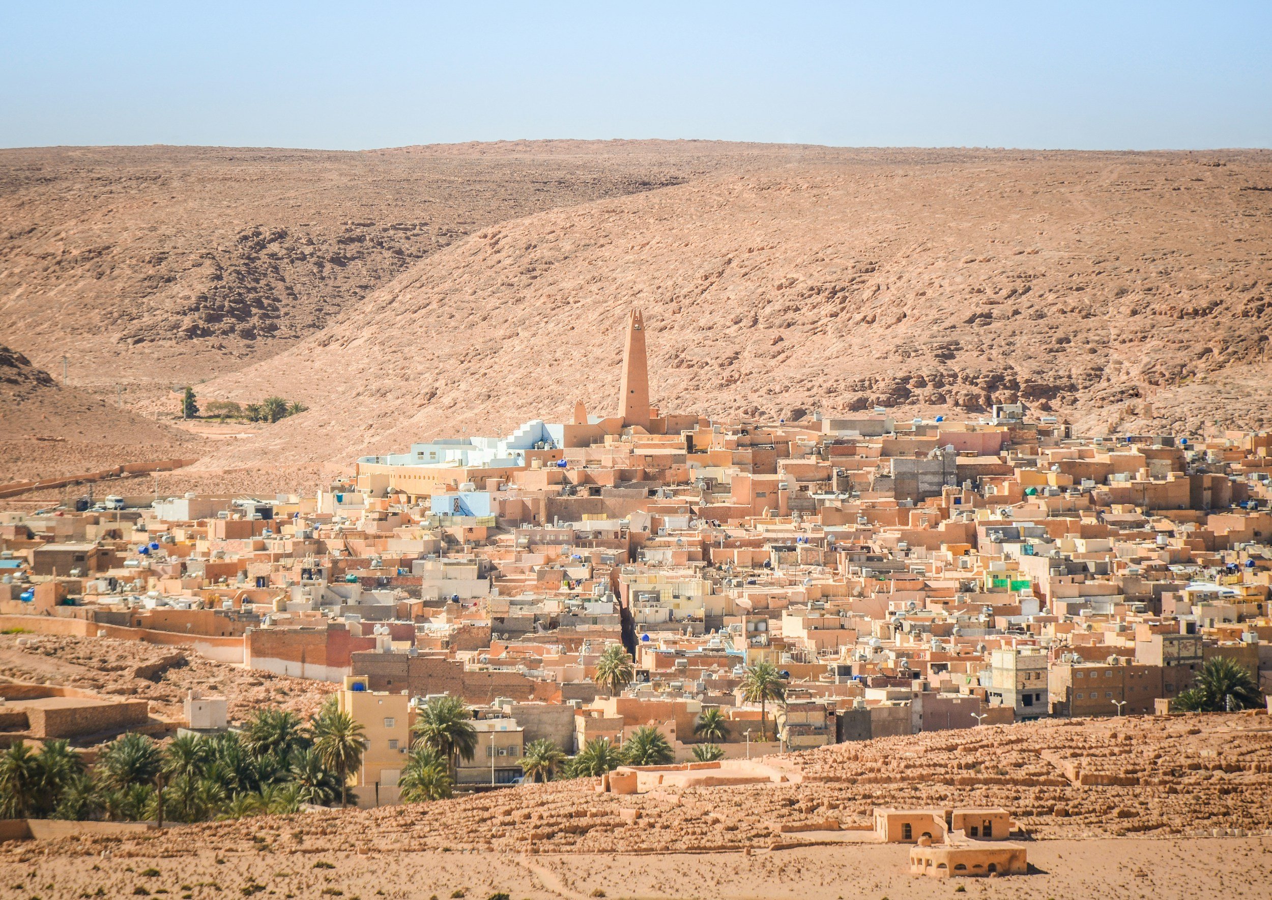 A desert town with adobe-style buildings surrounded by palm trees and barren mountains in the background.