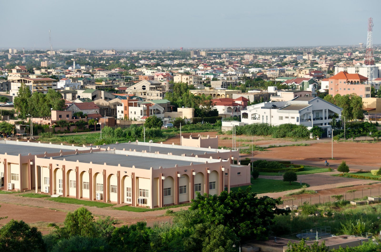 An aerial view of a city with various buildings, greenery, and open spaces under a clear sky.