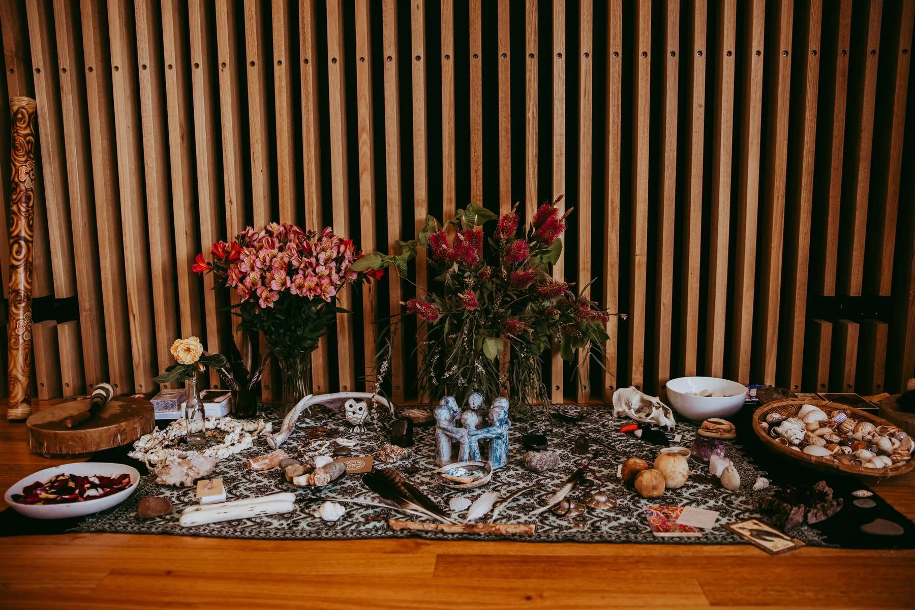 A table with various crystals, shells, flowers, and decorative objects against a wooden slatted wall.