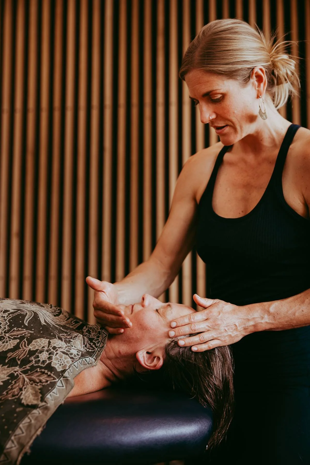 A woman performing facial massage on another woman lying on a massage table. 夏威夷按摩 Kahuna massage