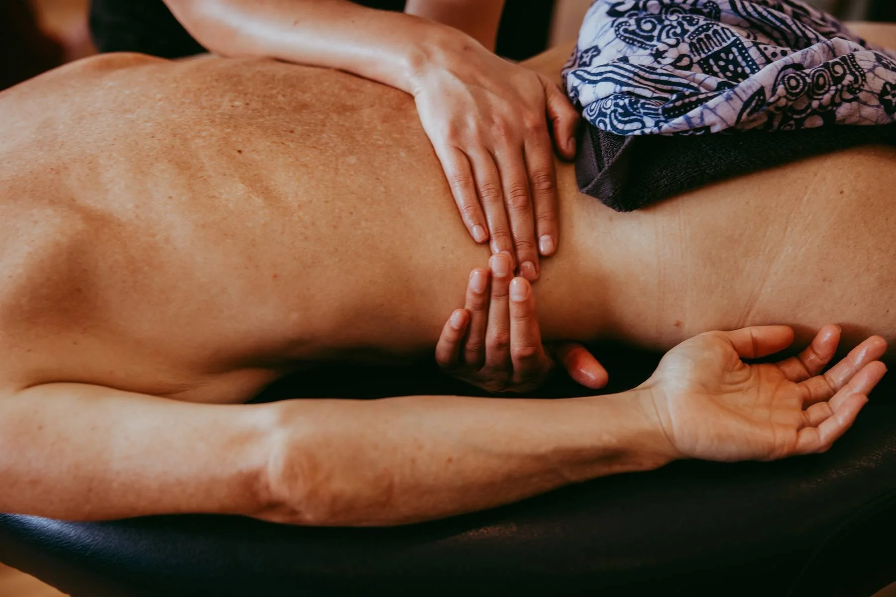 A person lying face down receiving a massage on their back, with multiple hands providing the massage. underbody massage 夏威夷按摩、Kahuna 按摩、腹部按摩、神聖、連結