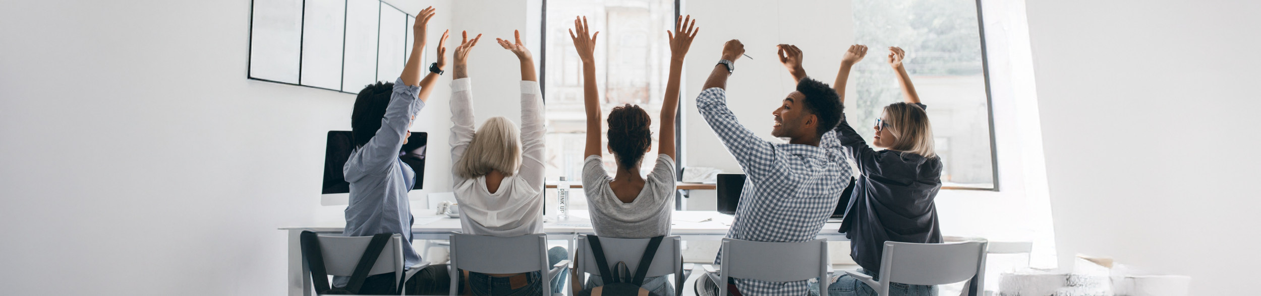 Group of diverse people with their hands raised in a meeting room with large windows.