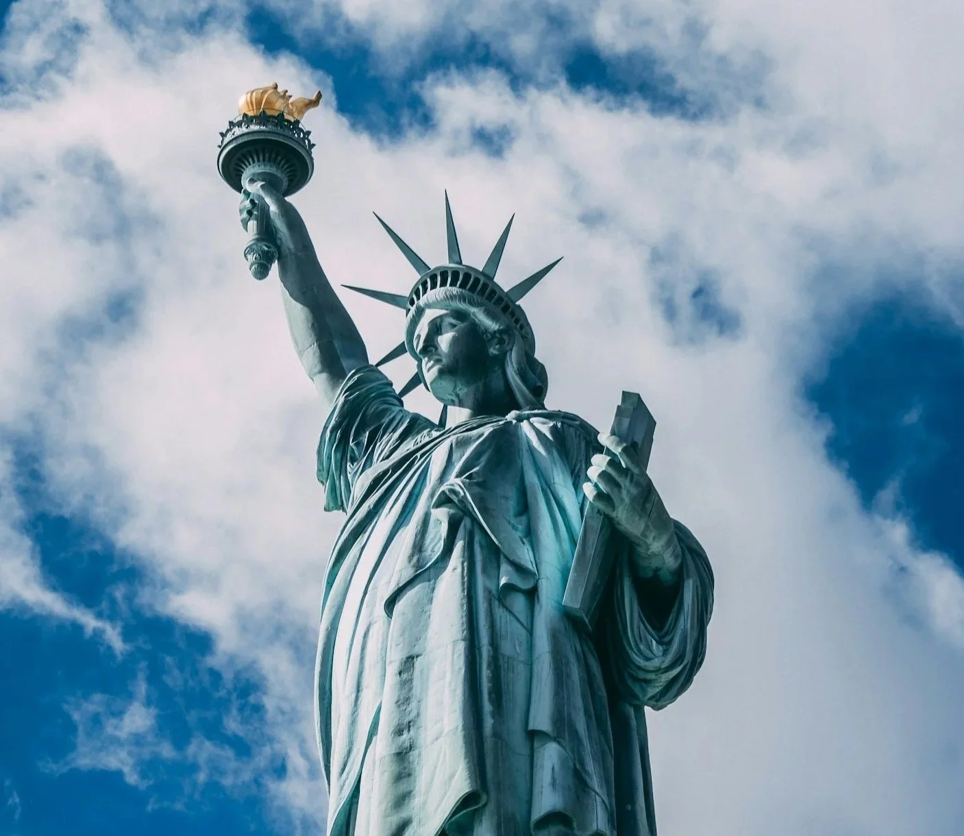 Upward view of the Statue of Liberty against a blue sky with scattered clouds.