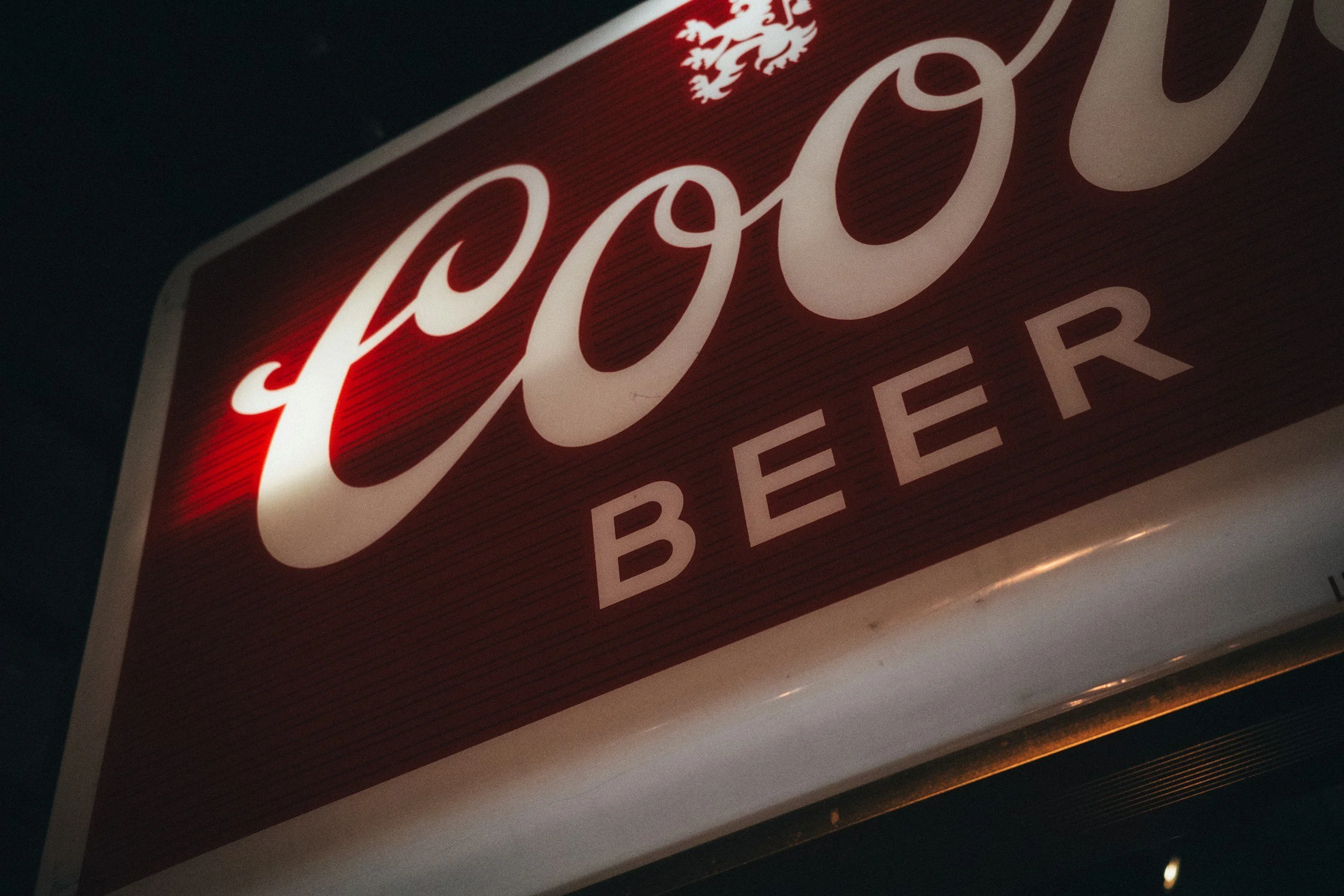 Nahaufnahme eines roten und weißen Werbeschilds mit der Aufschrift "Coop BEE" und einem kleinen Wappen darüber.