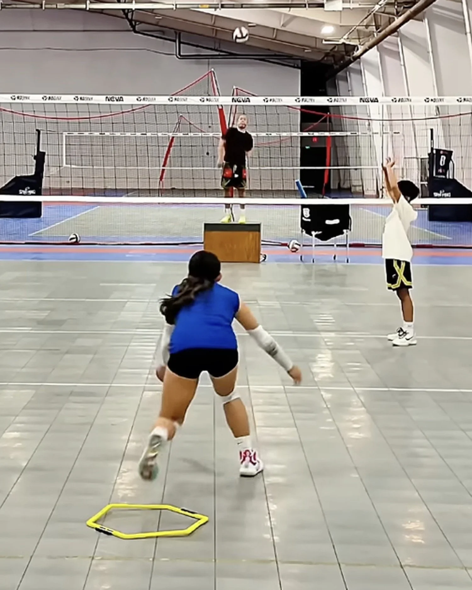 Athletes running an indoor volleyball drill near the net during training.