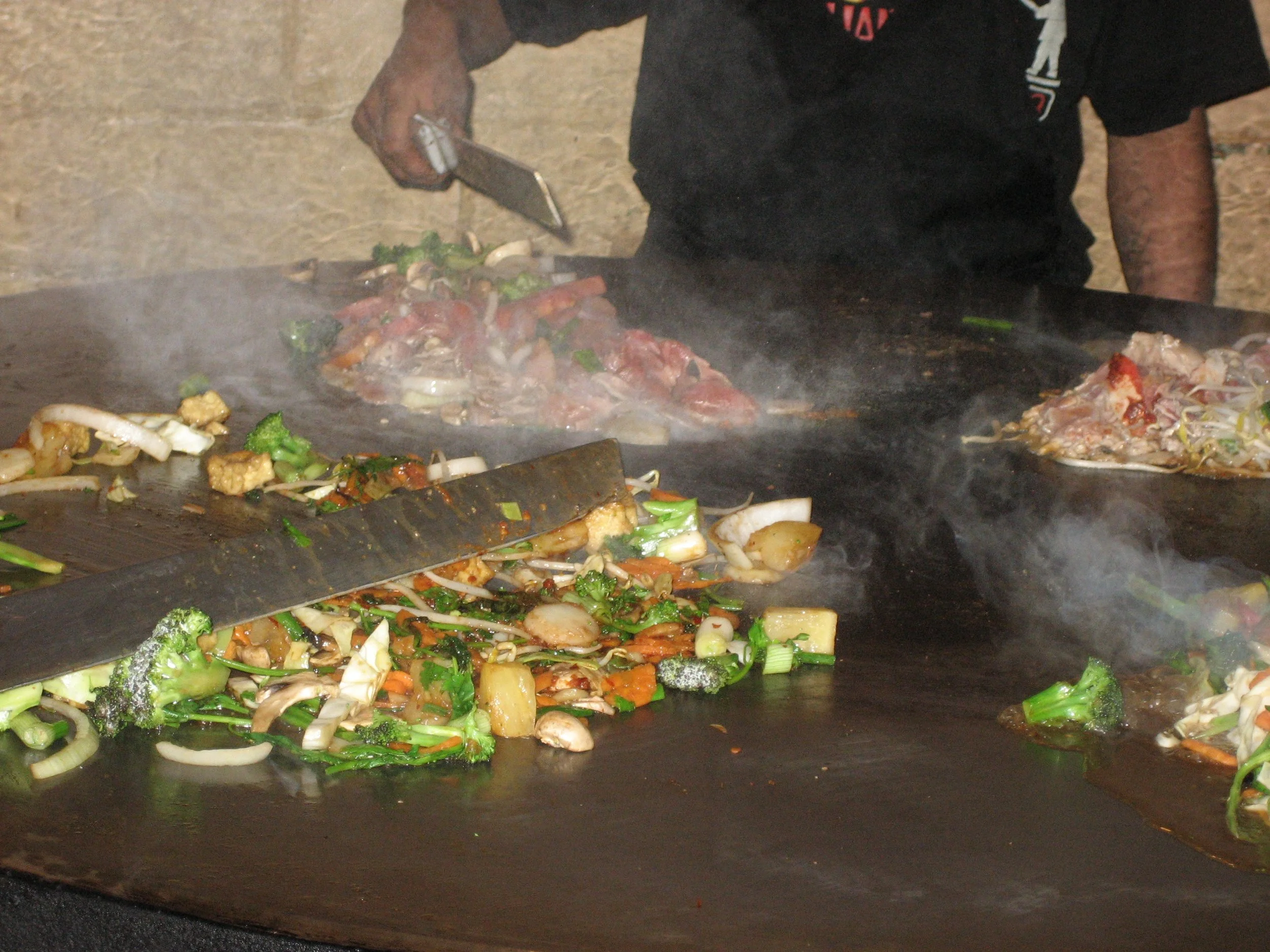 A chef cooking vegetables and meat on a large griddle.