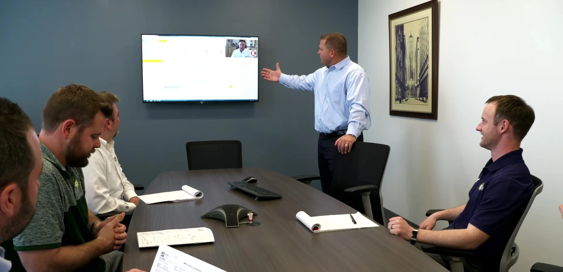 Man in board room gesturing to a screen in front of three others.