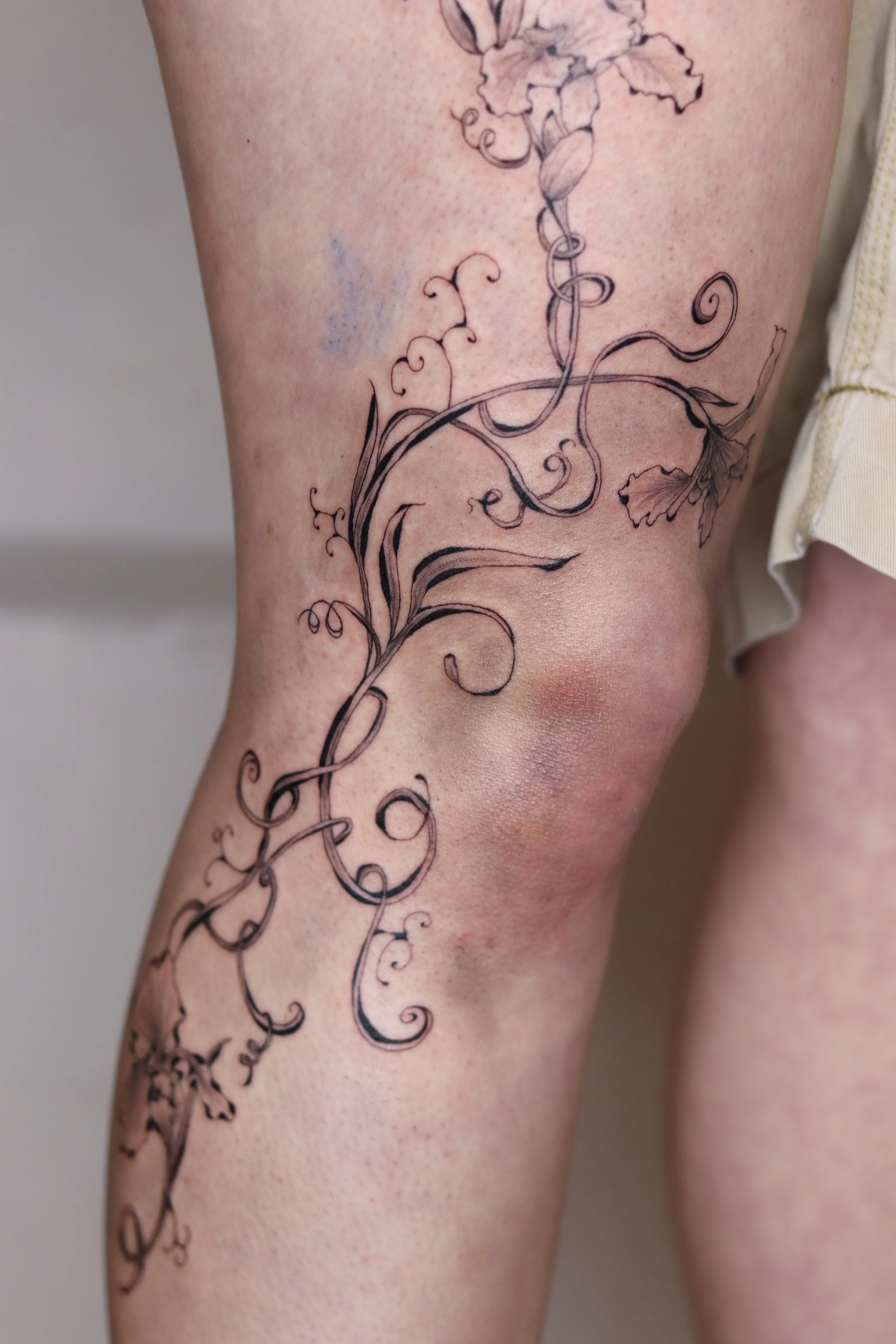 Tattoo of an artistic, flowing floral design with vines and leaves on a person's thigh.