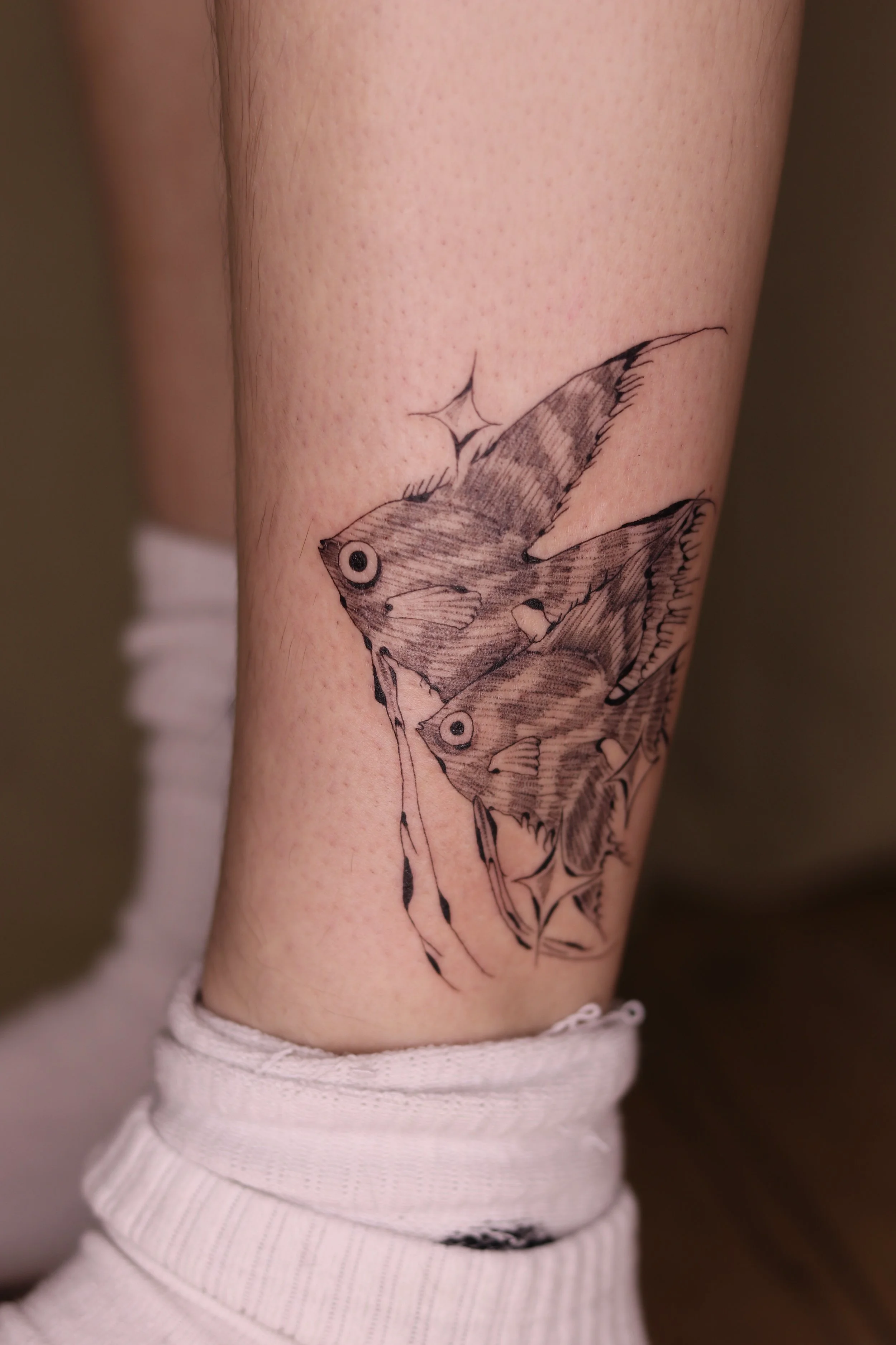Black and gray ink tattoo of two butterflies on a person's lower leg, with star-like sparkles nearby.