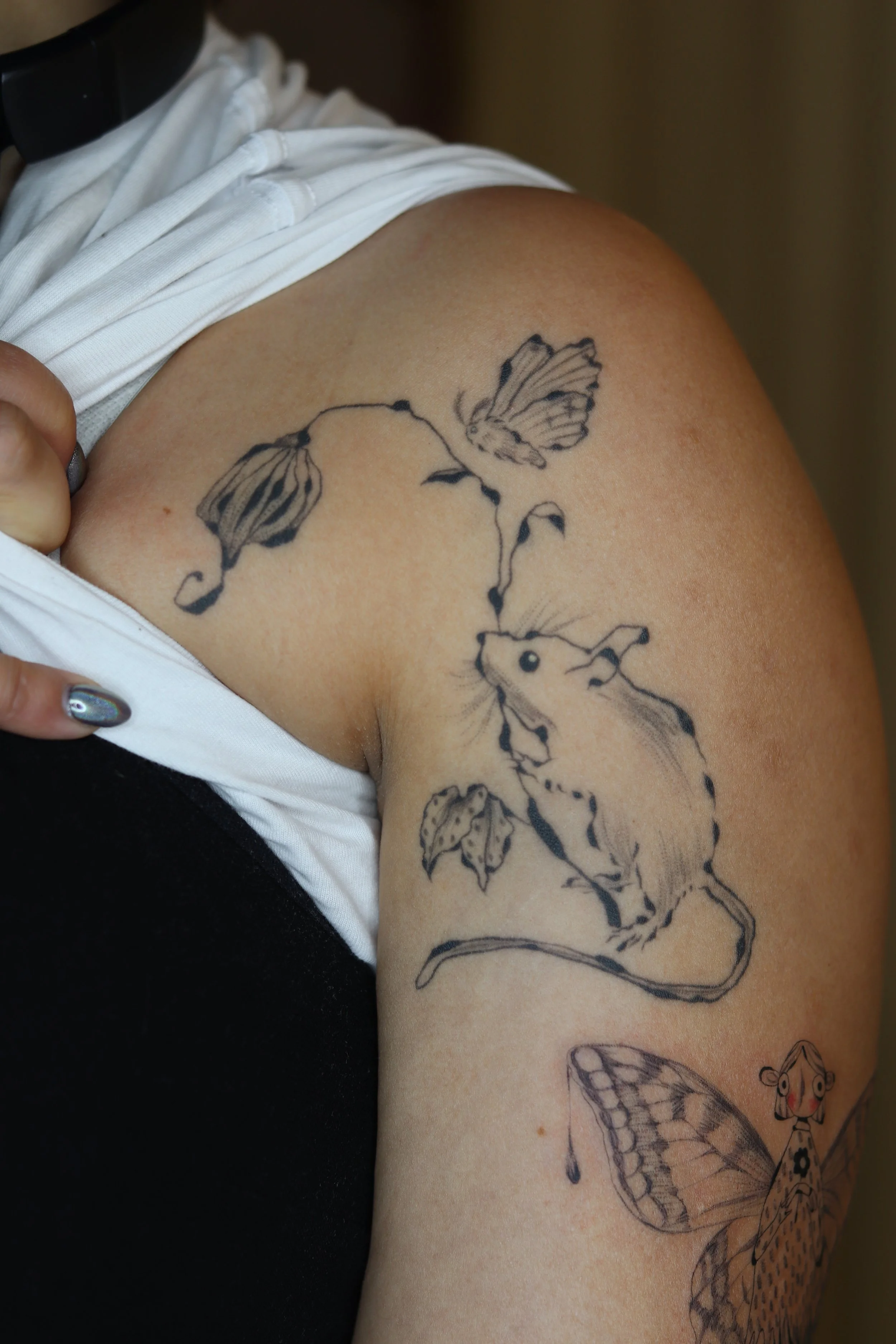 Tattoo of a mouse on the upper arm, connected to two butterflies with a branch, and a butterfly with detailed wings on the lower arm.