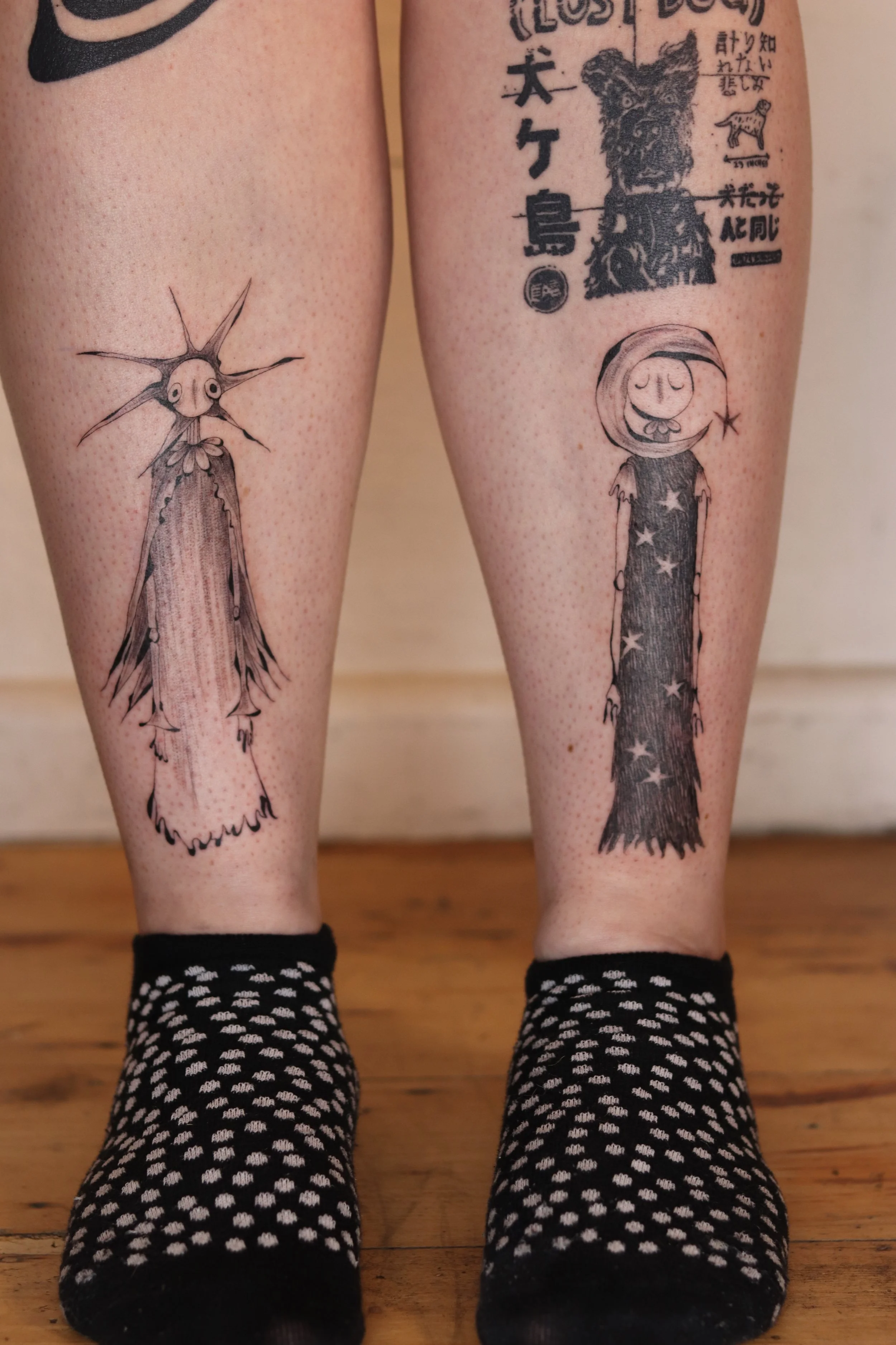 Tattoo of a cartoon girl in a starry dress on the right calf and a large spiky insect or crustacean on the left calf.