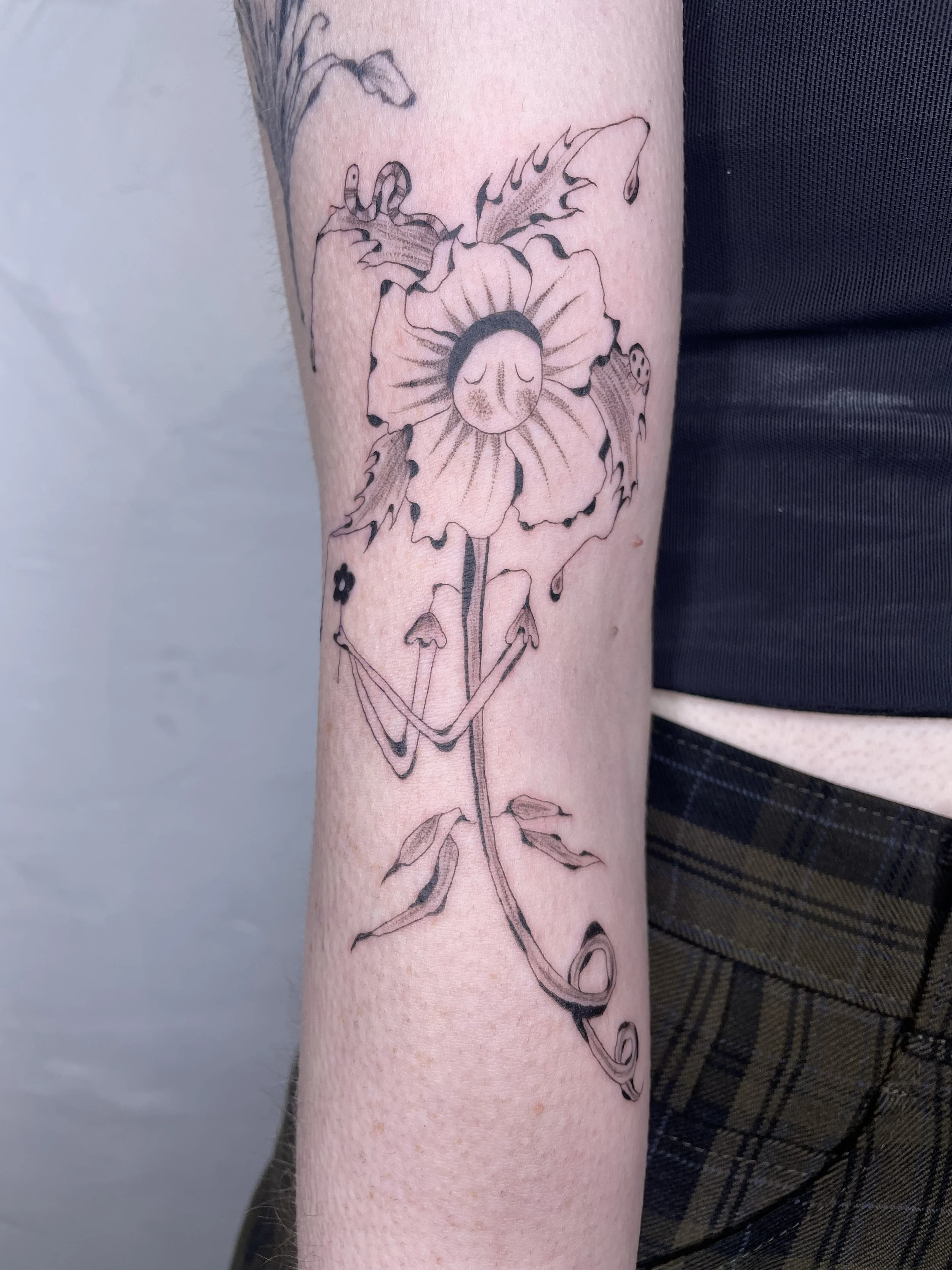 Tattoo of a flower with a face and a bokeh effect, with a smiling face on the flower's center, on a person's forearm.