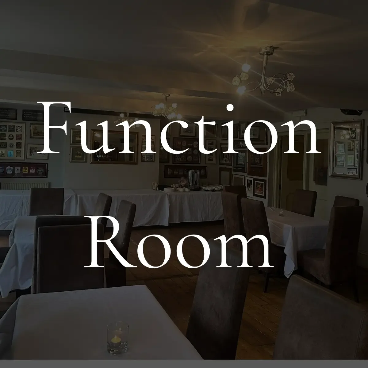 Interior of a dining room with tables covered in white tablecloths, chairs, and framed pictures on the walls.