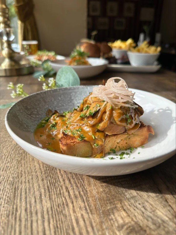 A bowl of steak and mushrooms with gravy, garnished with fresh herbs and fried onions, served on a rustic wooden table.