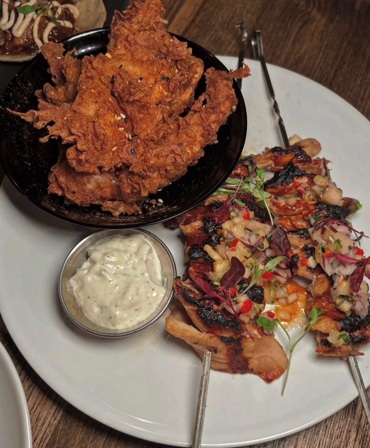 Plate with fried chicken, fried fish fillets topped with chopped vegetables and herbs, and a small dish of tartar sauce.