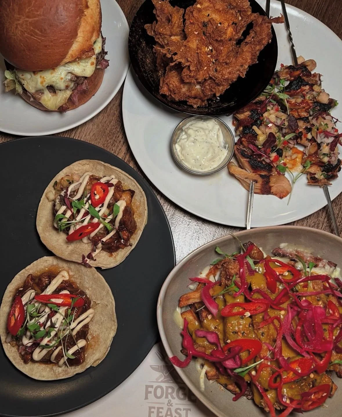 A variety of dishes including burgers, tacos, fried chicken, and salads with colorful toppings on plates