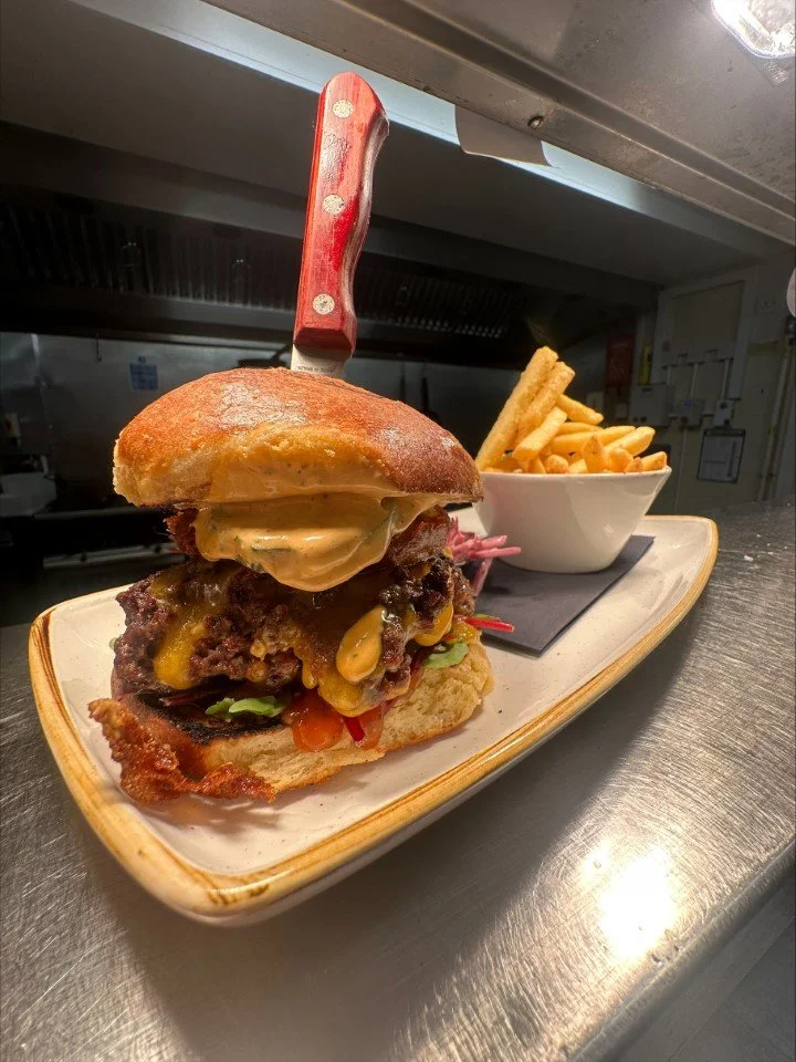 A burger with a bun, melted cheese, lettuce, and a beef patty, served with a side of French fries in a white bowl on a rectangular plate.