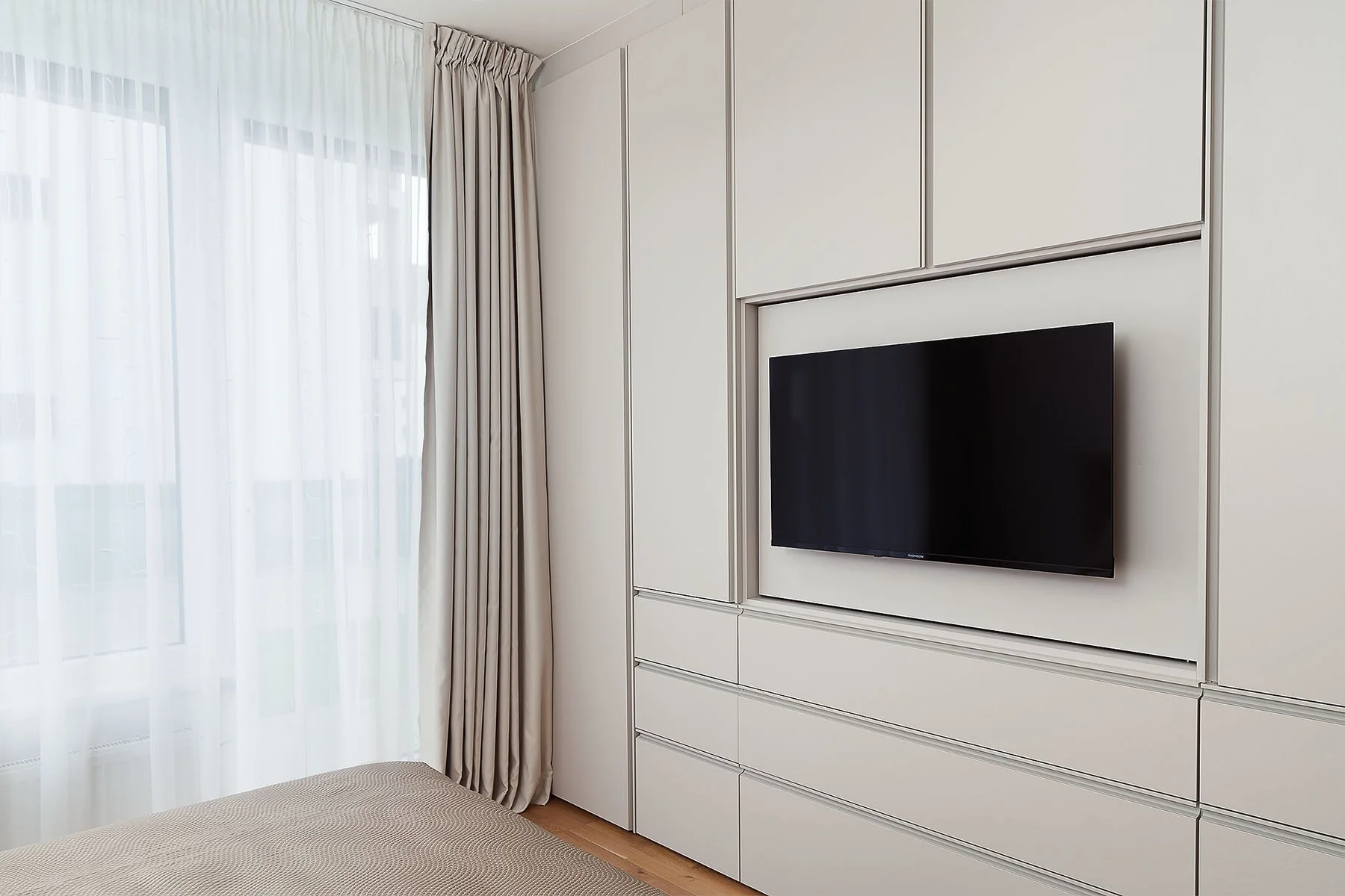 Snímek interiéru ložnice s integrovanou televizí ve vestavěné stěně.