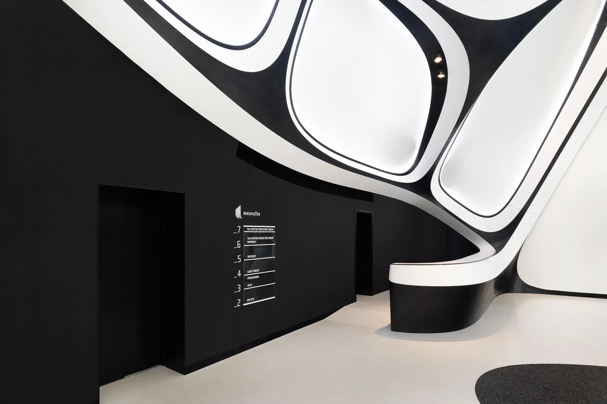Organicky tvarované černo-bílé schodiště a futuristický design lobby s čistými liniemi.
