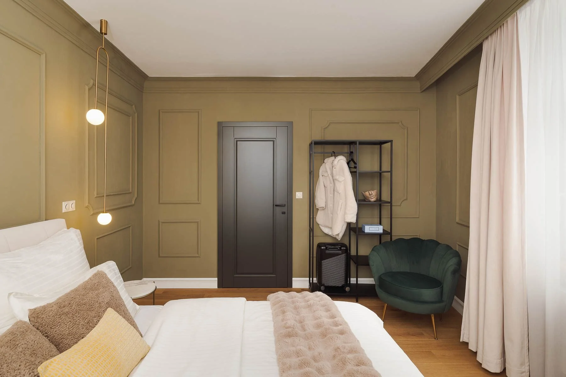 Elegantní ložnice s olivově zelenou stěnou, designovými kulatými svítidly a otevřeným úložným systémem.