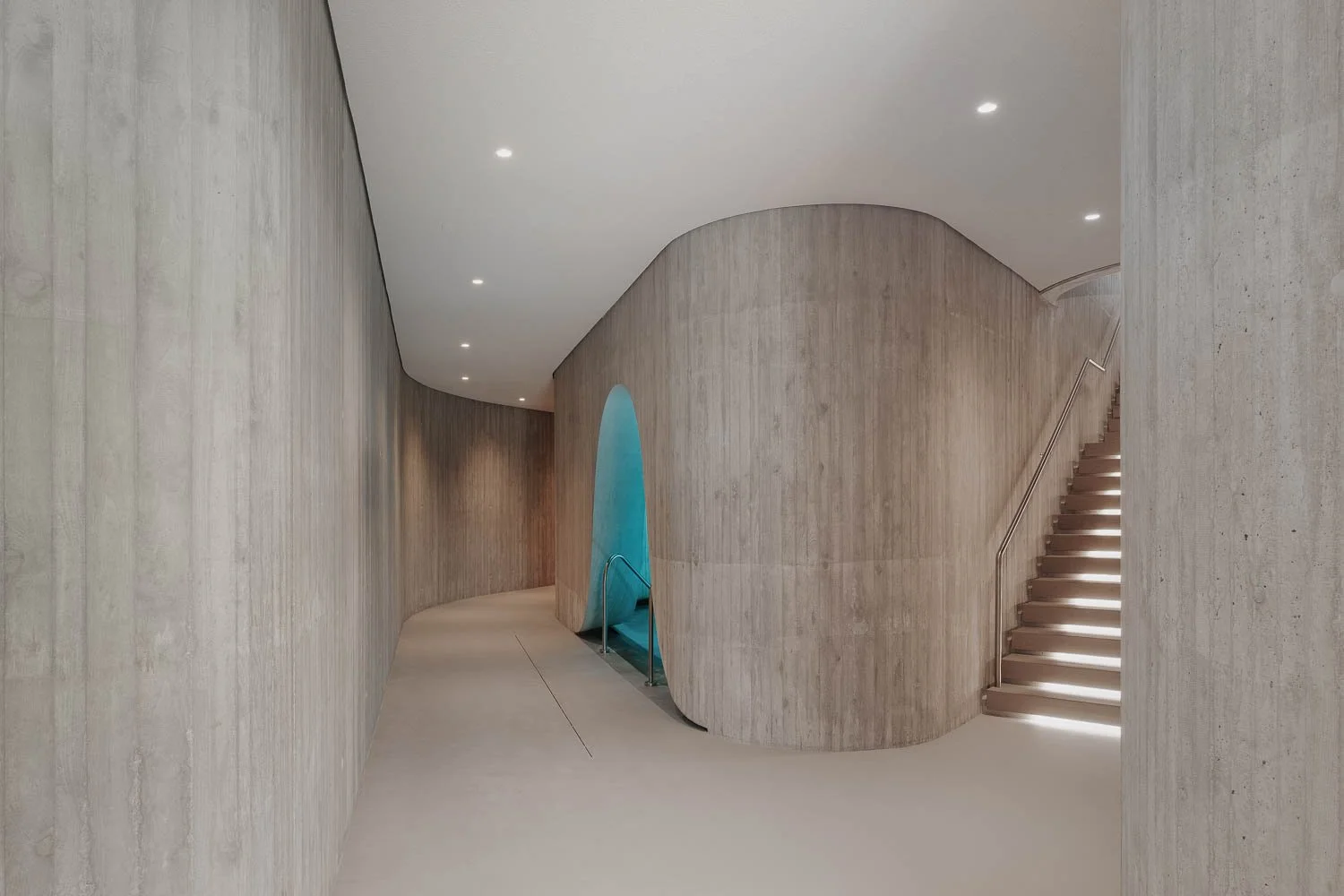 Průchod s organicky tvarovanými stěnami z pohledového betonu a náladovým podsvícením v rakouském wellness.