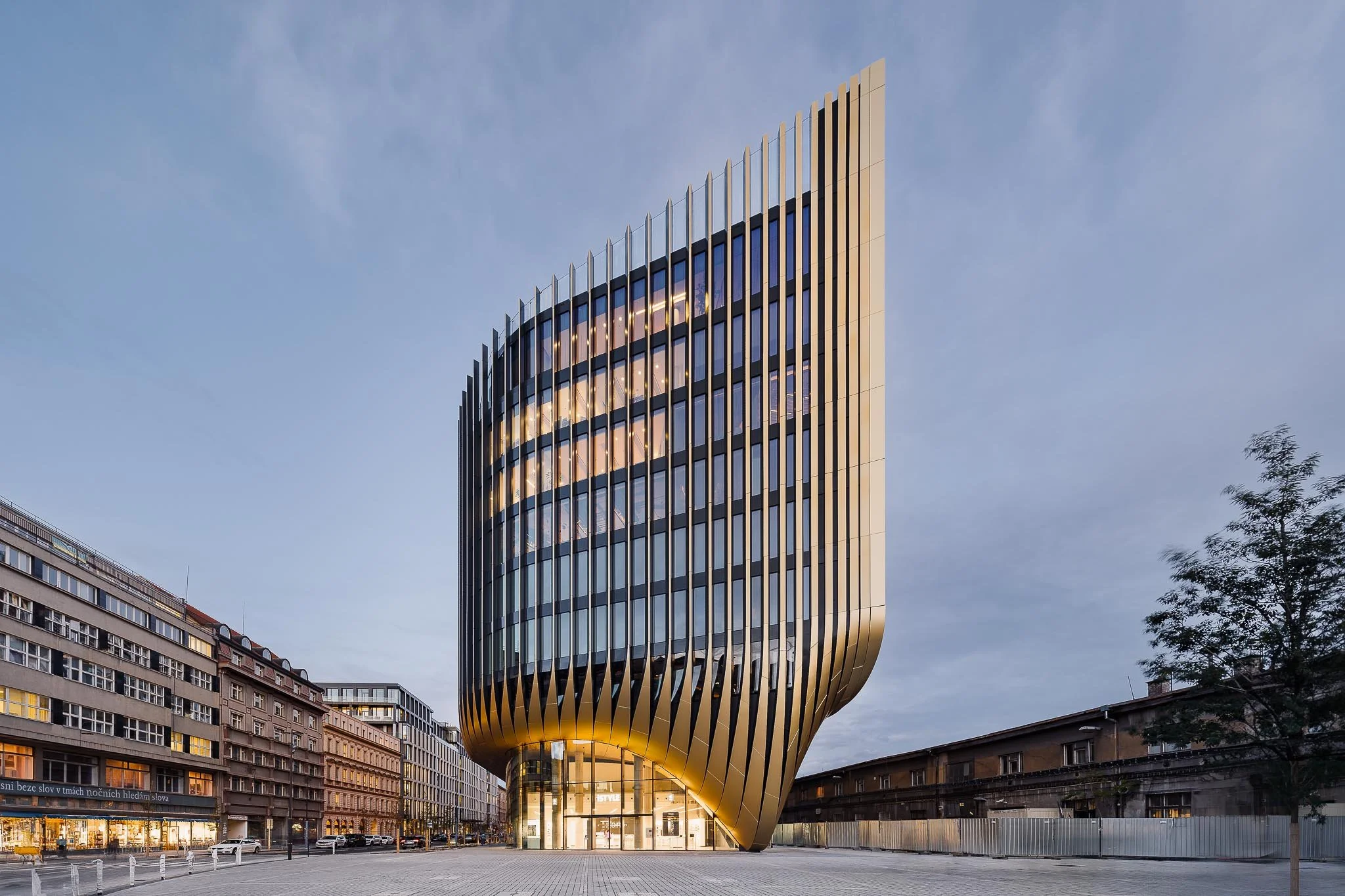 Pohled na ikonickou stavbu od Zaha Hadid Architects s jejími typickými zlatými lamelami a organicky tvarovaným nárožím.