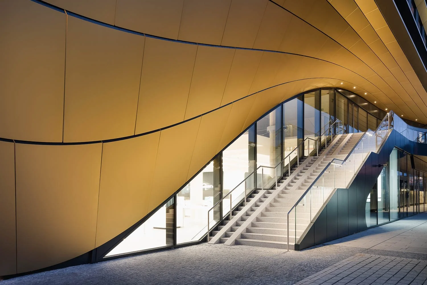 Exteriérové schodiště budovy Masaryčka pod převisem zlaté lamelové fasády.
