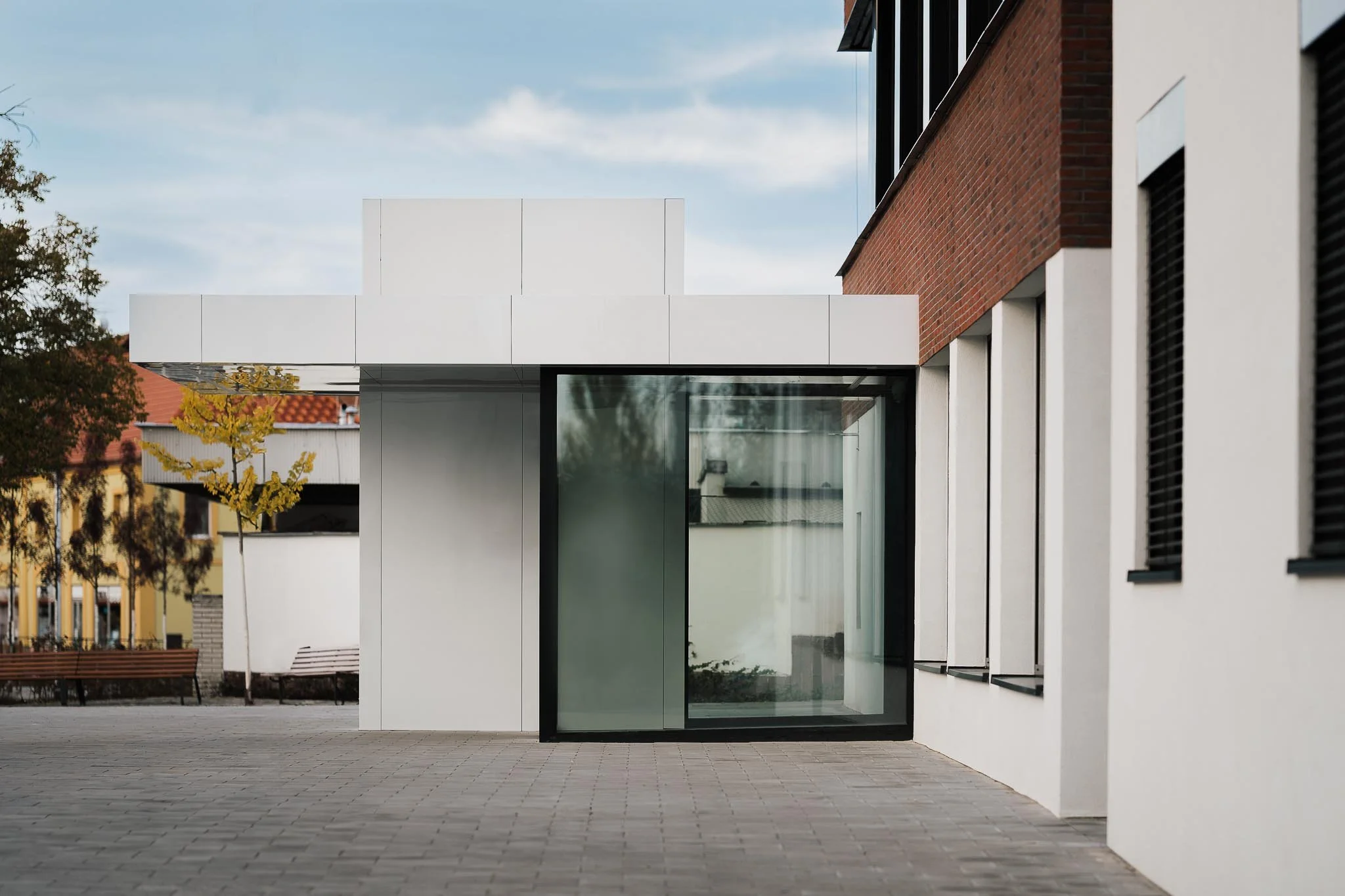 Čistý architektonický detail bílé moderní budovy s velkoformátovým prosklením a černými rámy.