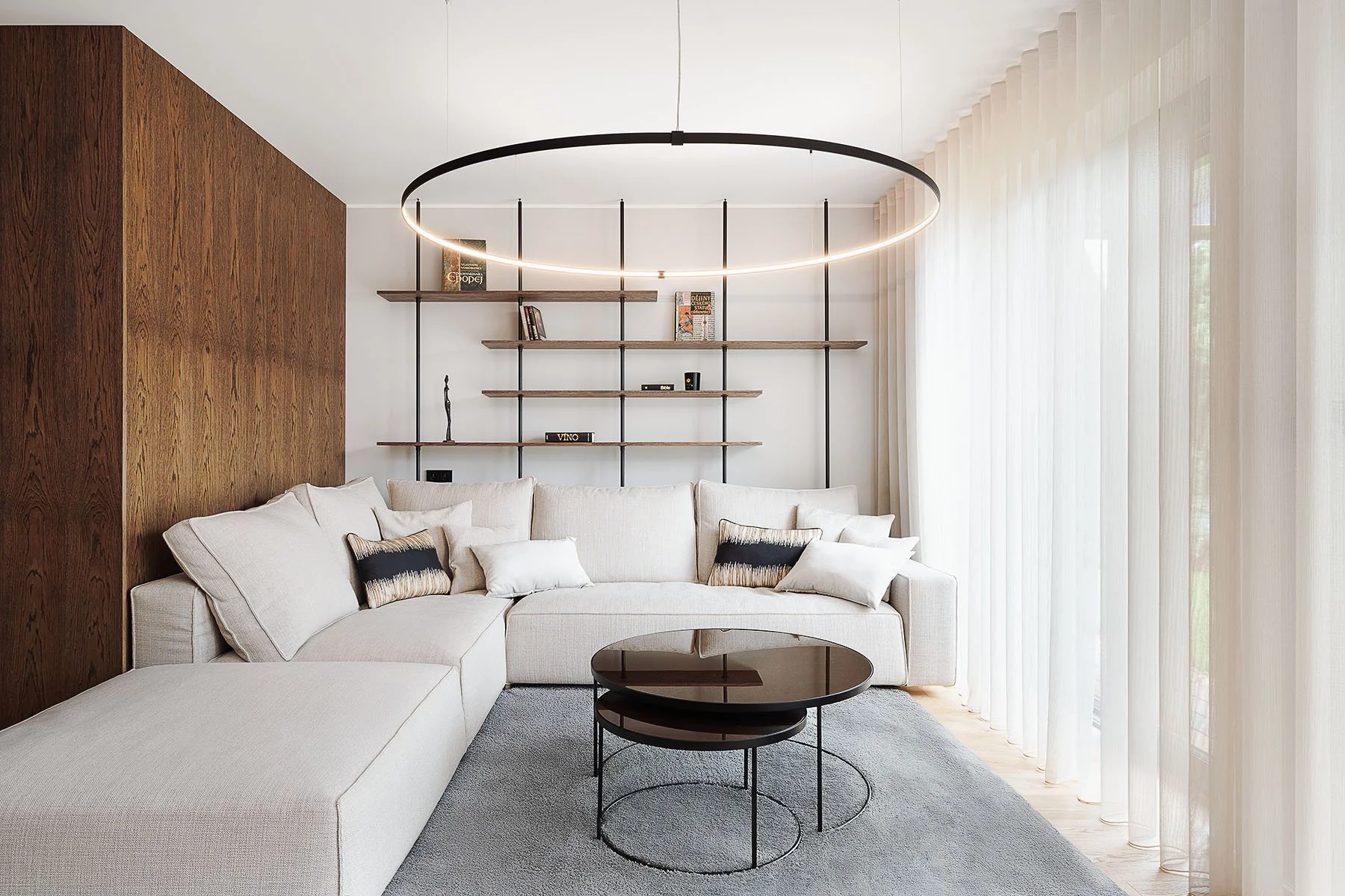 Světlý interiér obývacího pokoje s bílou rohovou pohovkou, minimalistickými policemi a designovým kruhovým svítidlem.
