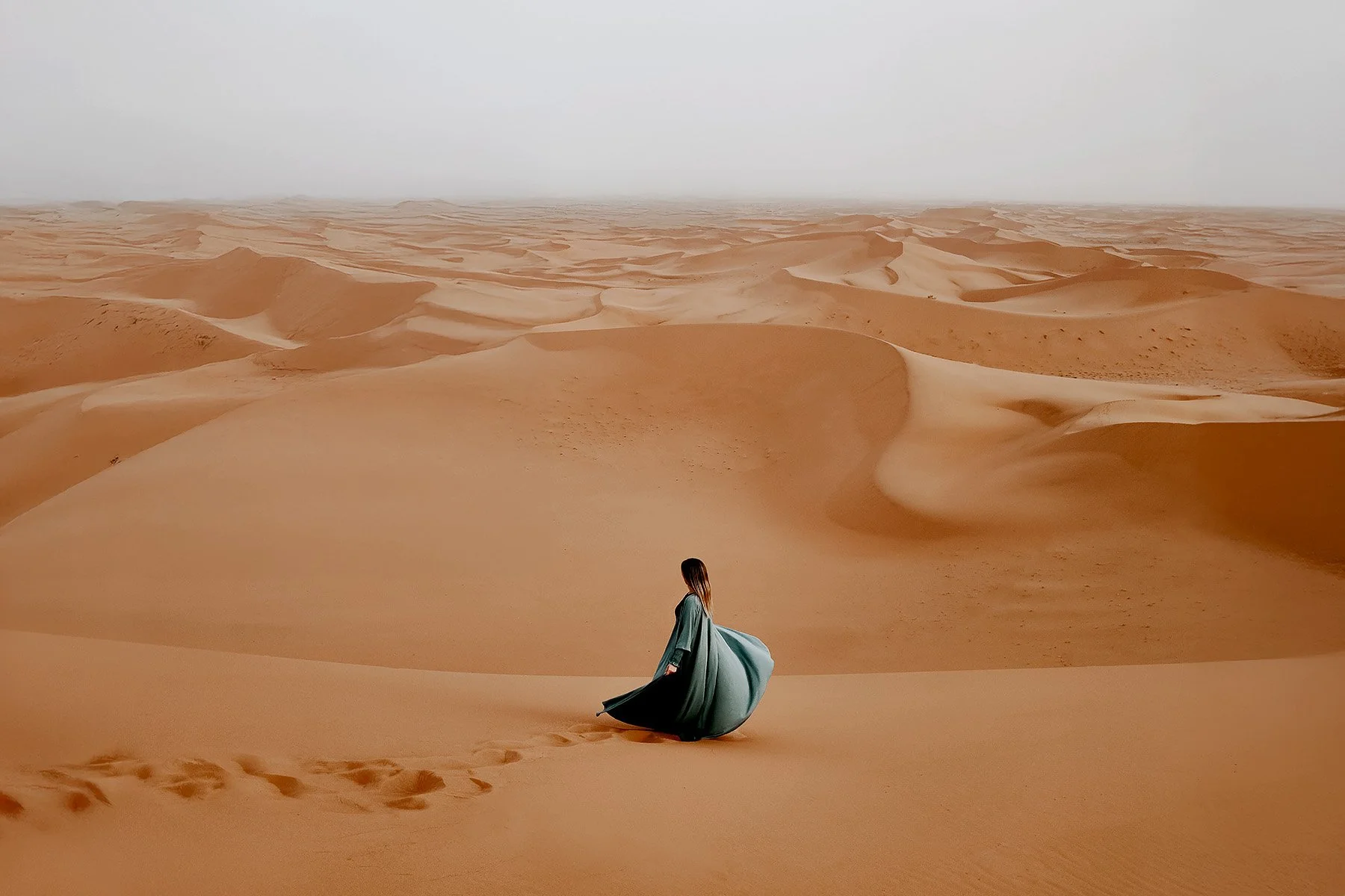 Písečné duny v poušti při západu slunce s postavou v tradičním oděvu v Saúdské Arábii.