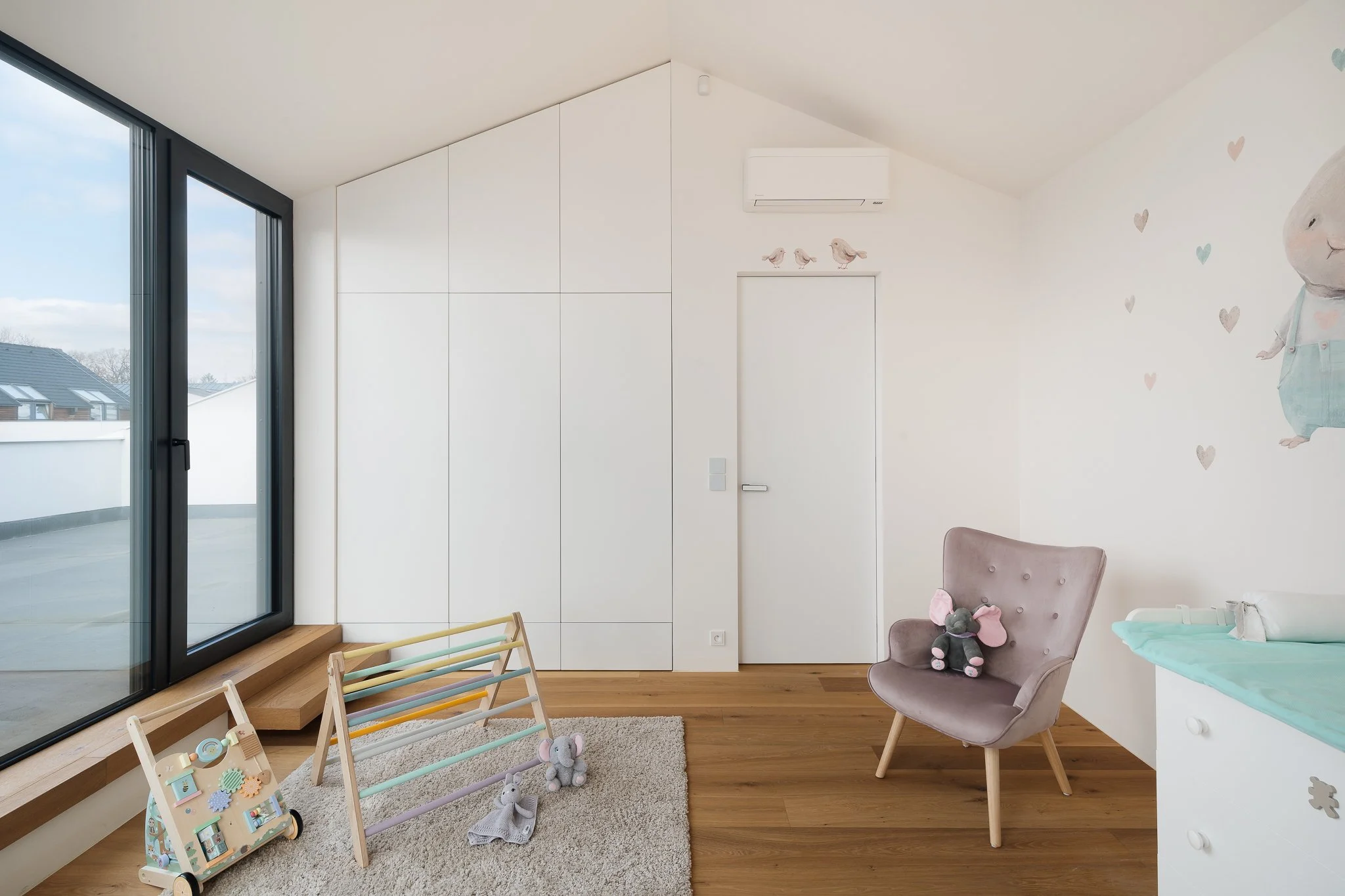 Minimalistický interiér dětského pokoje v jemných barvách s designovým křesílkem a dřevěnými prvky.