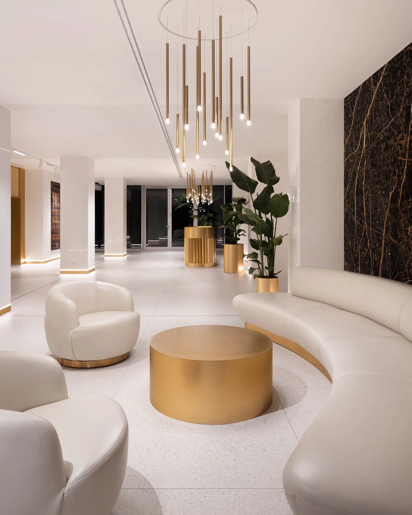 Designová lobby s bílými pohovkami, zlatým stolkem, závěsnými svítidly a mramorovou zdí.