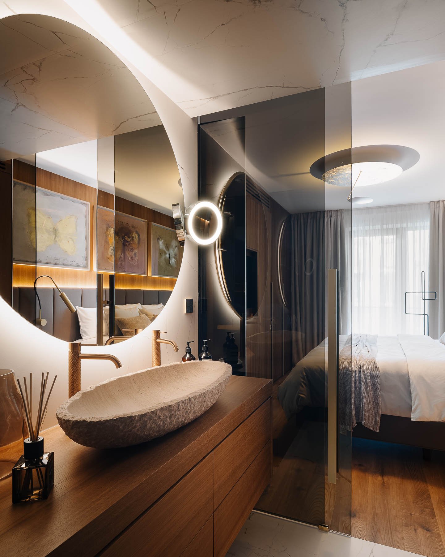 Moderní koupelna s kamenným umyvadlem na dřevěné desce. Prosklená příčka navazuje na elegantní ložnici.