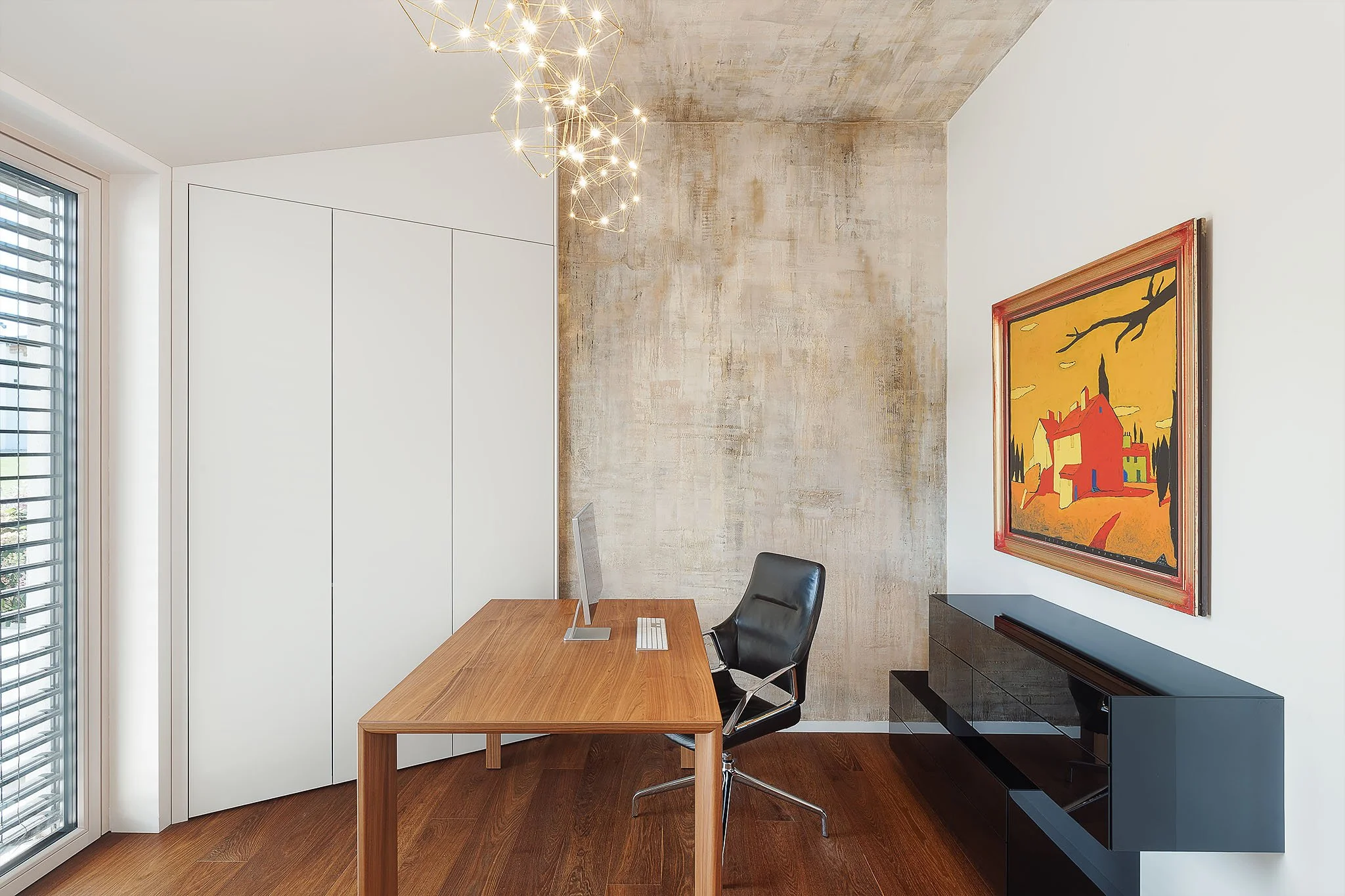 Designová domácí pracovna s masivním dřevěným stolem a texturovanou betonovou stěnou.