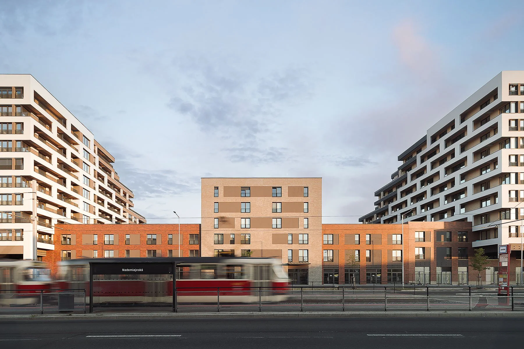 Městská architektura bytového domu s cihlovou fasádou a projíždějící tramvají v popředí.