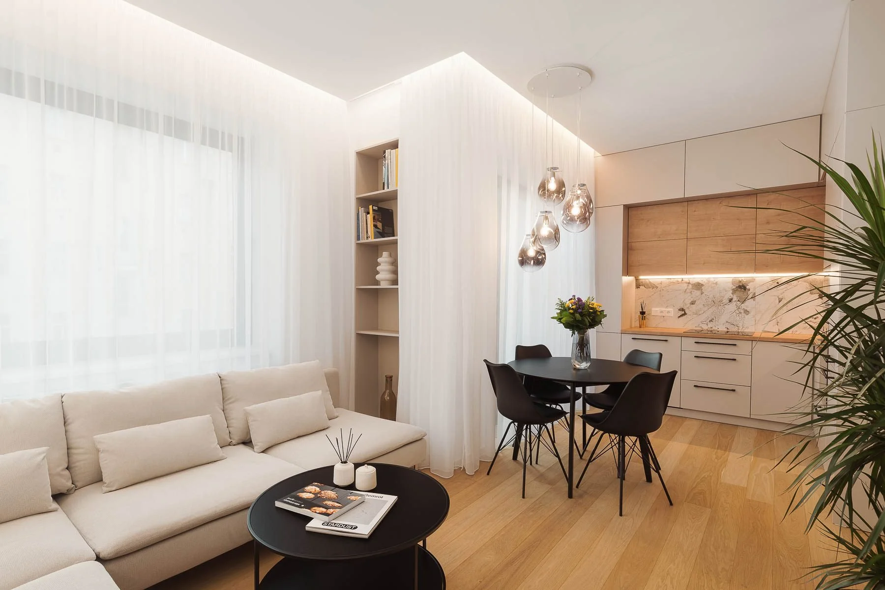 Designový moderní interiér obývacího pokoje a kuchyně se světlými podlahami, béžovou pohovkou a černými stolky.